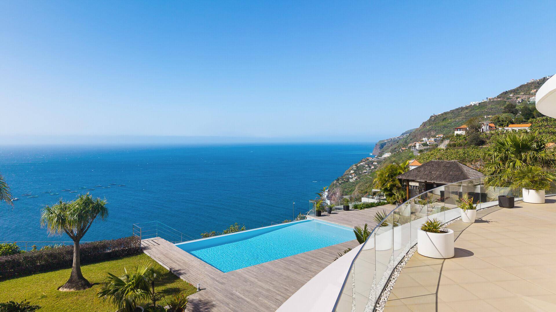 Geräumige Terrasse mit Infinity-Pool, Holzdeck und Glasgeländer, bietet einen weiten Blick auf das Meer.