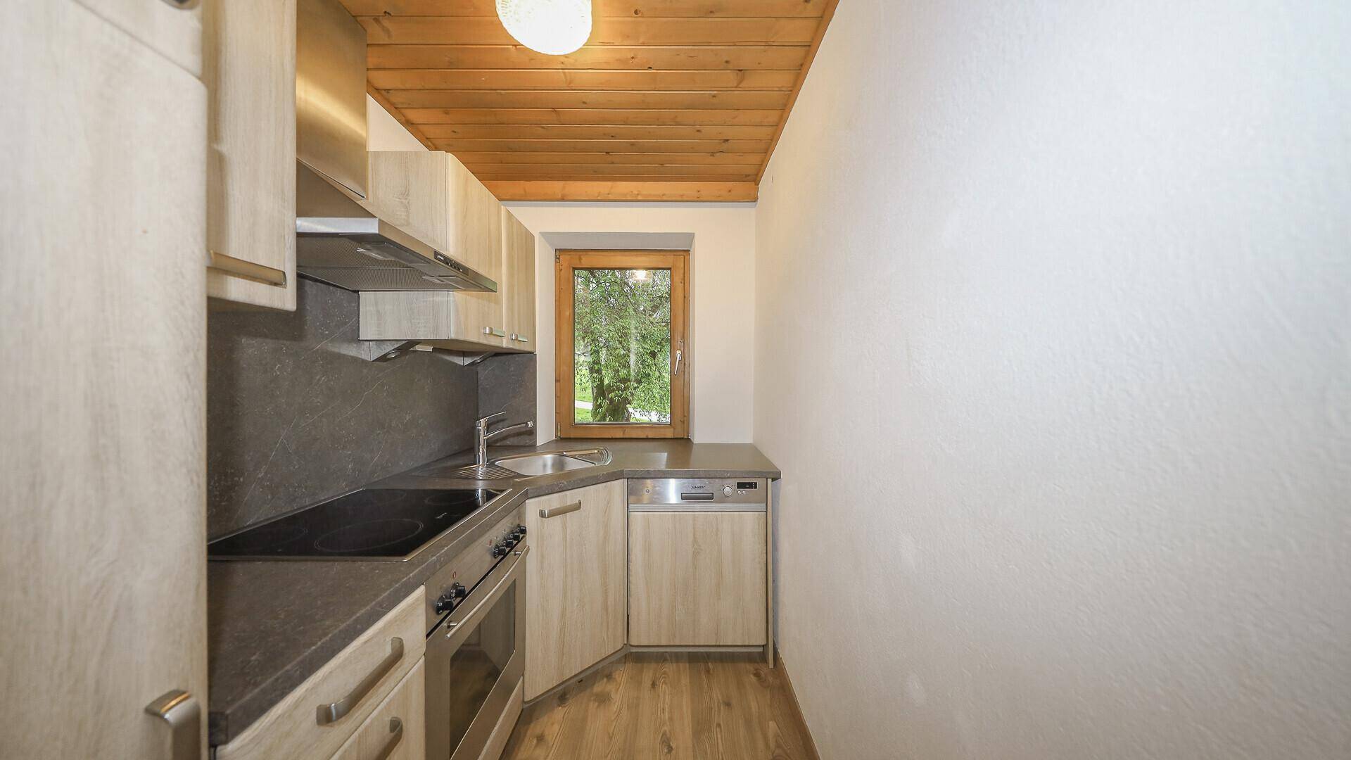 Kleine, funktionale Küche mit hellen Holzschränken, Einbaugeräten und Fenster.