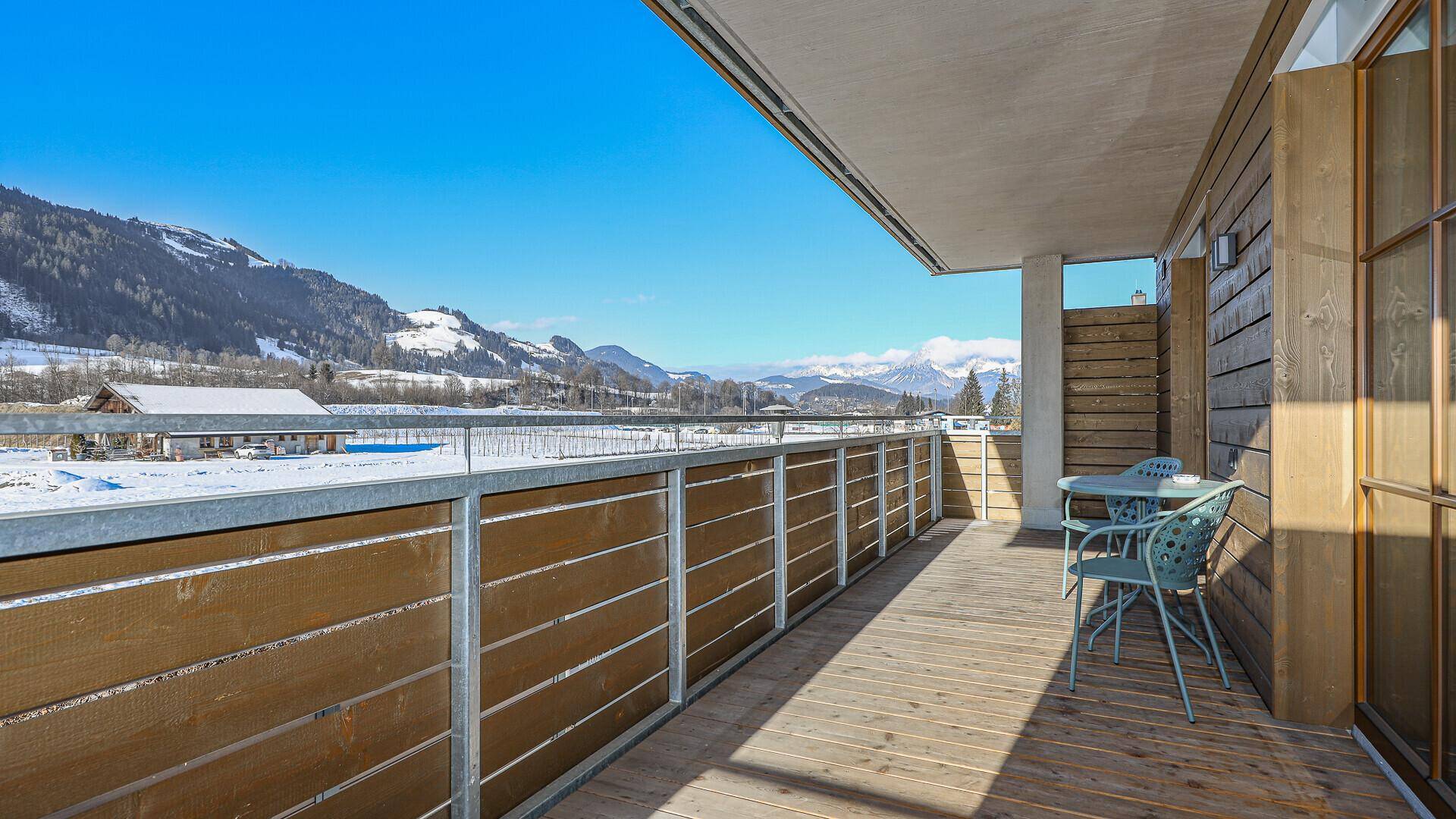 Geräumiger Balkon mit Holzboden, Sitzgelegenheiten und einem weiten Blick auf die verschneite Berglandschaft.