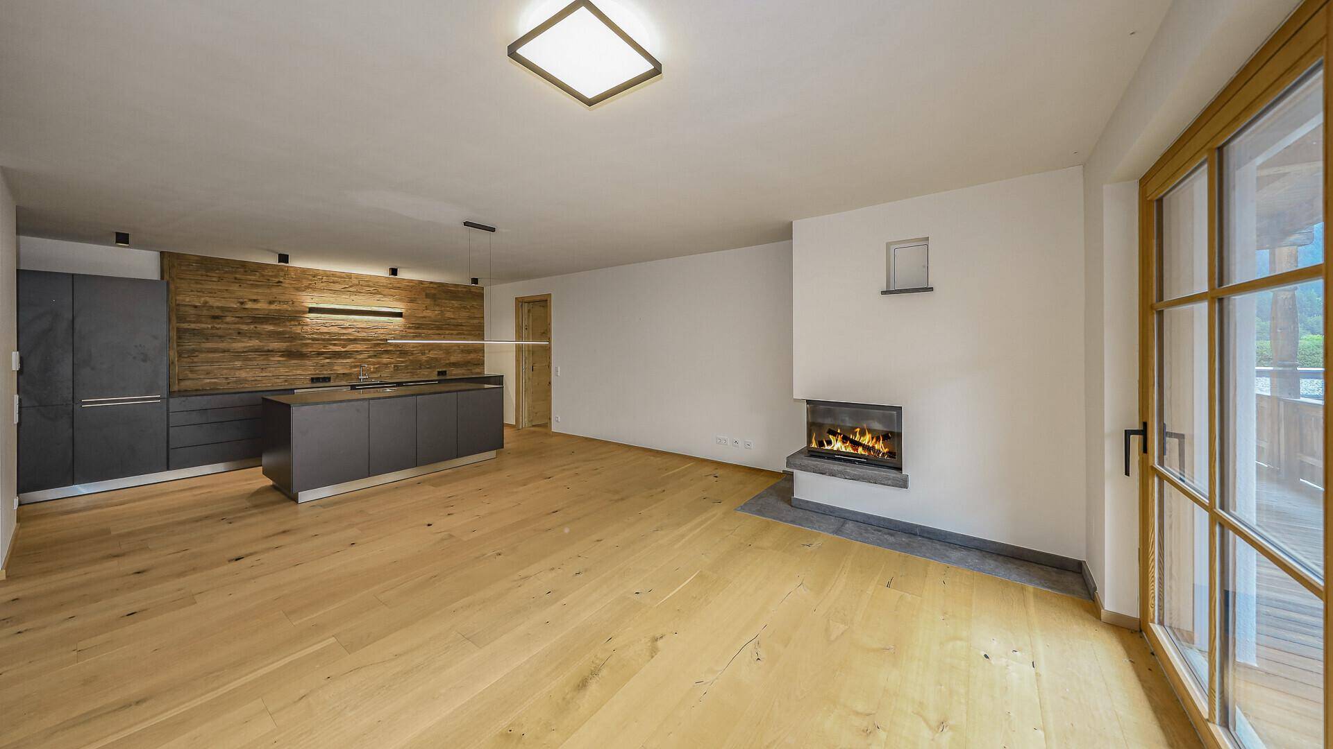 Offener Wohnbereich mit Holzboden, Kamin und moderner Küche.