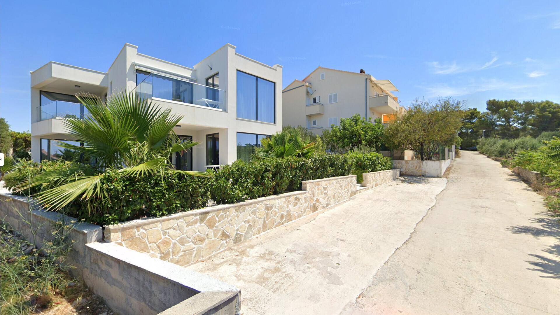 Moderne Villa mit mediterraner Bepflanzung und Zufahrt, umgeben von natürlicher Landschaft.