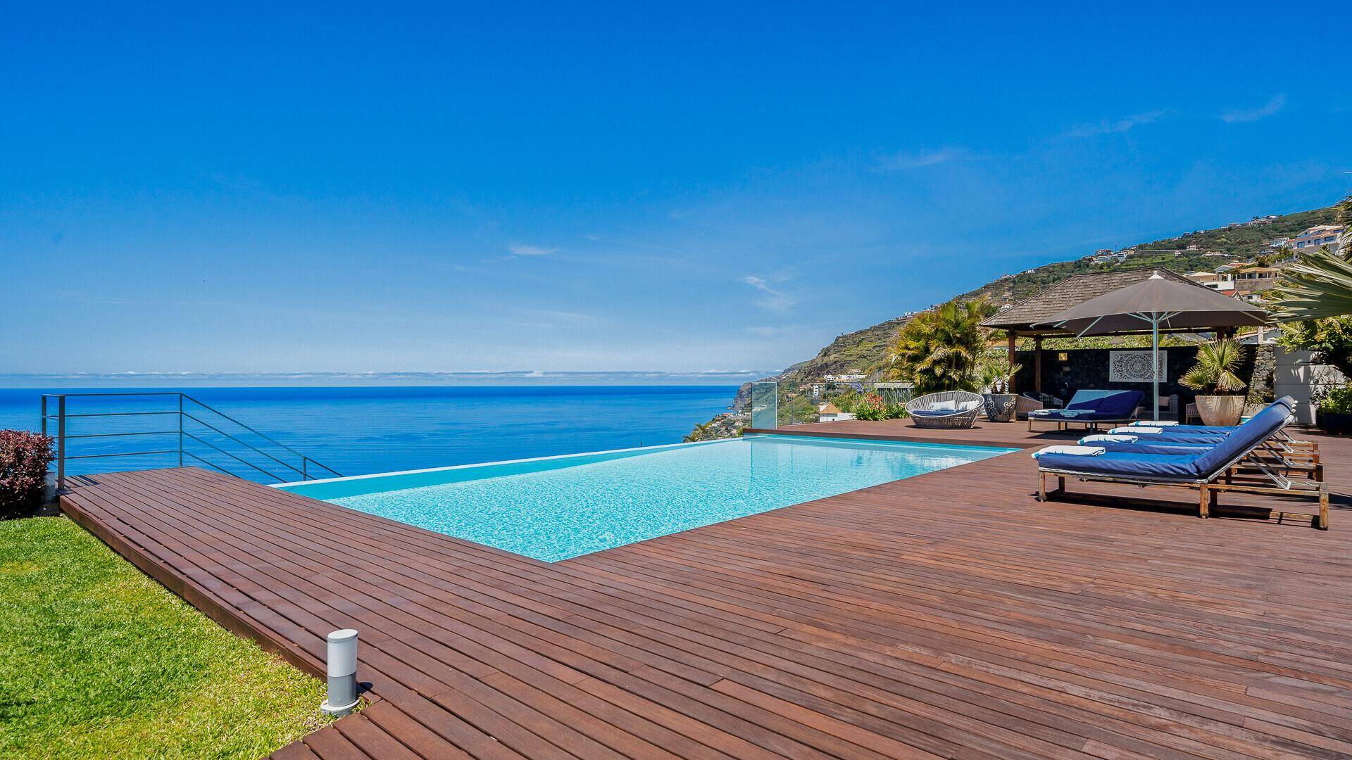 Infinity-Pool mit Holzdeck, Sonnenliegen und schattigem Sitzbereich, bietet einen unverbauten Blick auf das Meer.