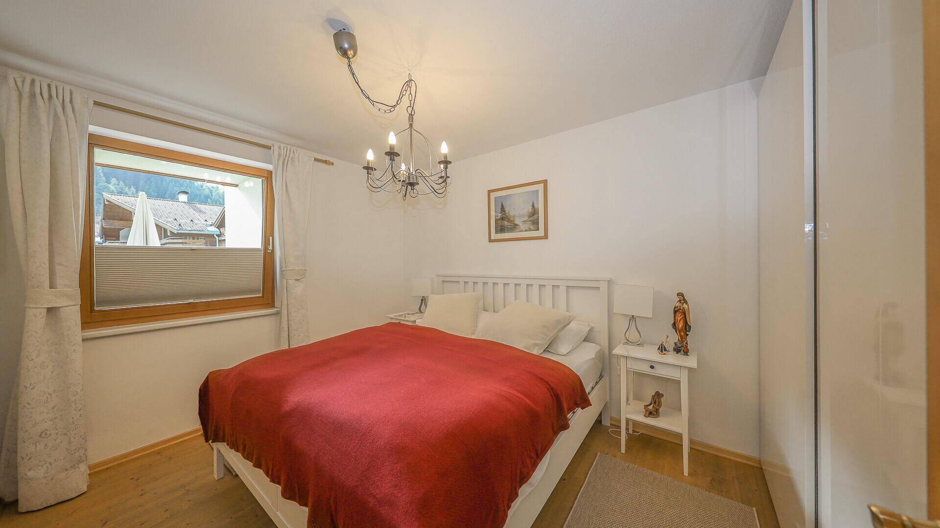 Schlafzimmer mit weißem Bett, Holzboden und Fenster mit Blick nach draußen.