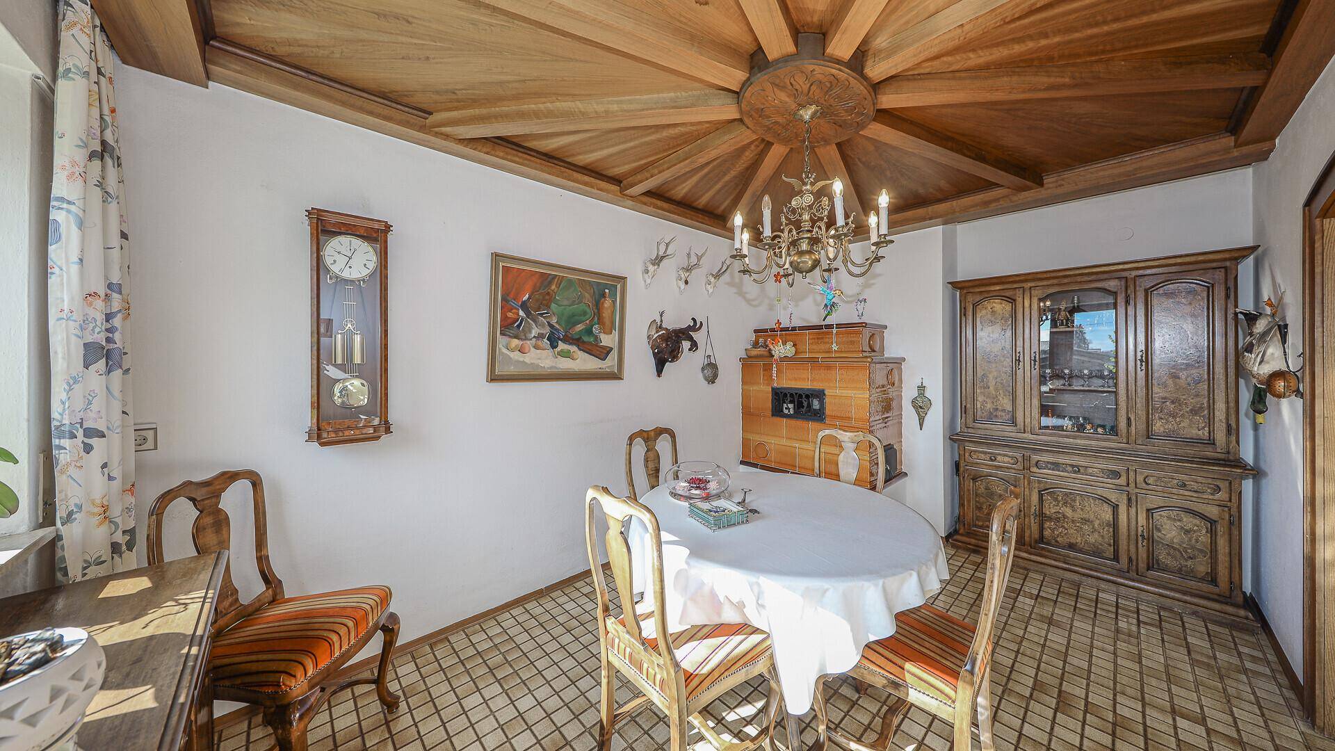 Traditioneller Essbereich mit Holztisch, Kachelofen und dekorativer Holzdecke.