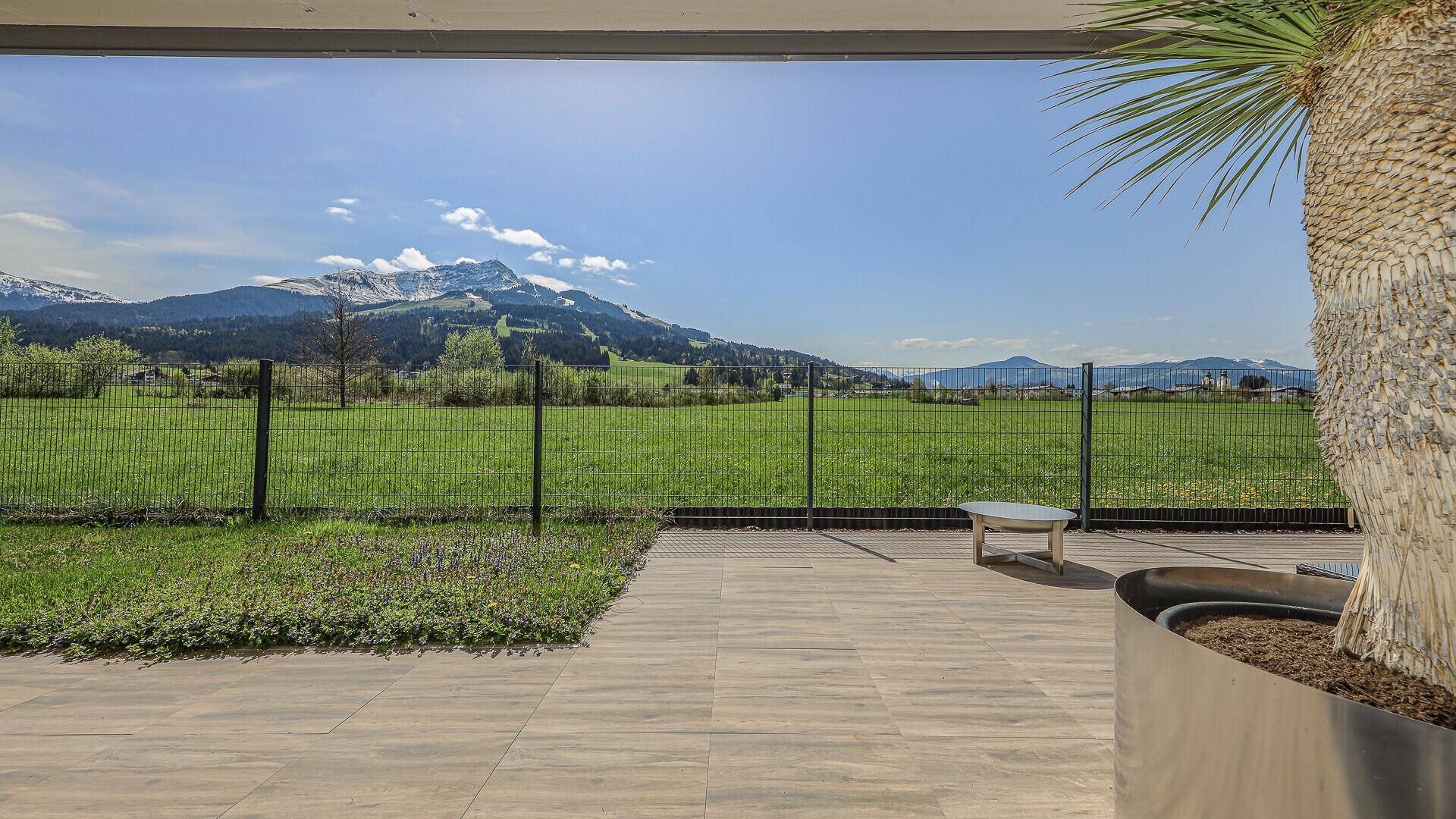 Ruhige Terrasse mit Blick auf die weite grüne Wiese und die beeindruckende Bergkulisse in der Ferne.
