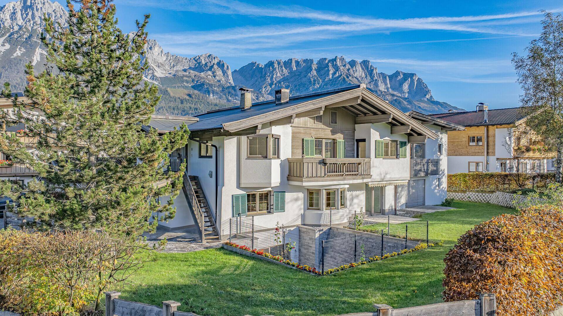 Alpines Wohnhaus mit weißer Fassade, grünen Fensterläden und Bergblick in sonniger Lage.