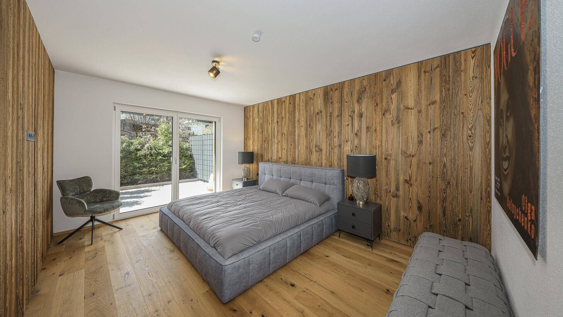 Gemütliches Schlafzimmer mit Holzwand, Doppelbett und Zugang zu einem Außenbereich.
