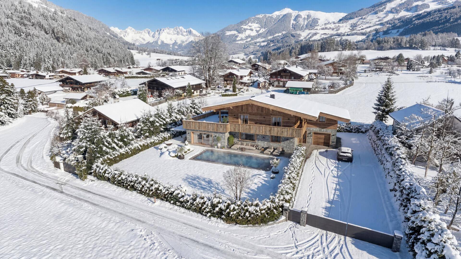 Winterliche Luftaufnahme eines exklusiven Chalets mit verschneitem Garten und Pool in den Bergen.