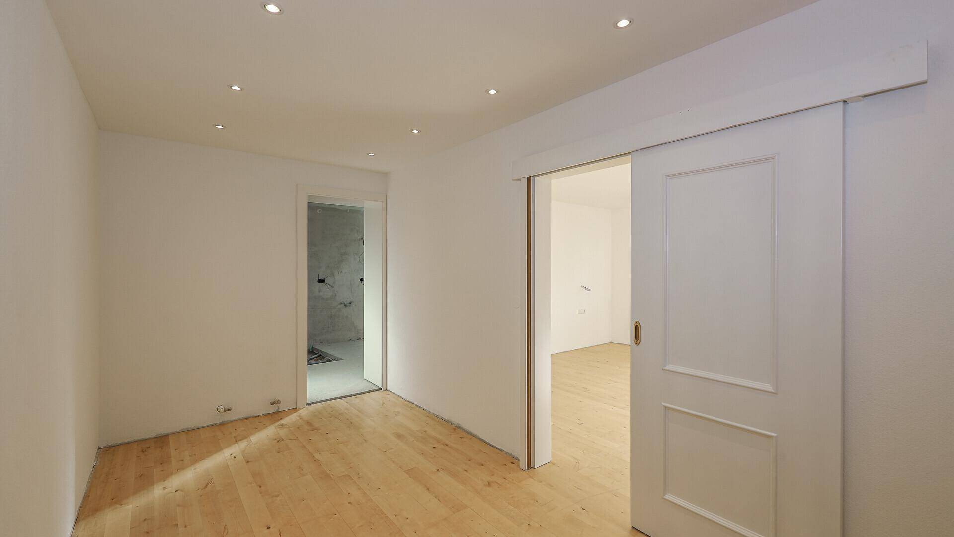 Heller Raum mit Holzboden und Schiebetür, ideal als begehbarer Kleiderschrank oder Abstellraum.