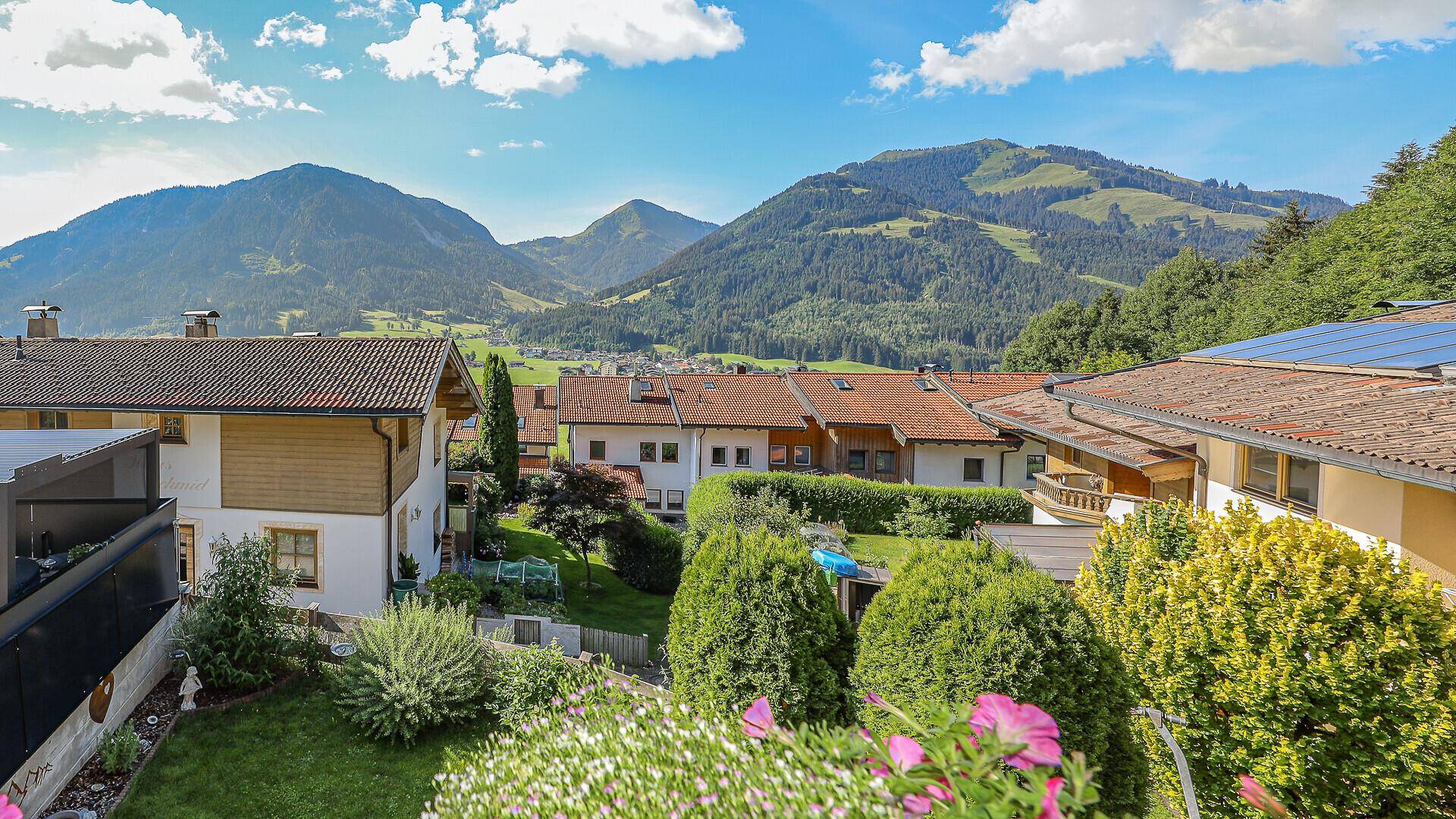 Panoramablick über die Dächer der Nachbarschaft mit grünen Gärten und majestätischen Bergen im Hintergrund.