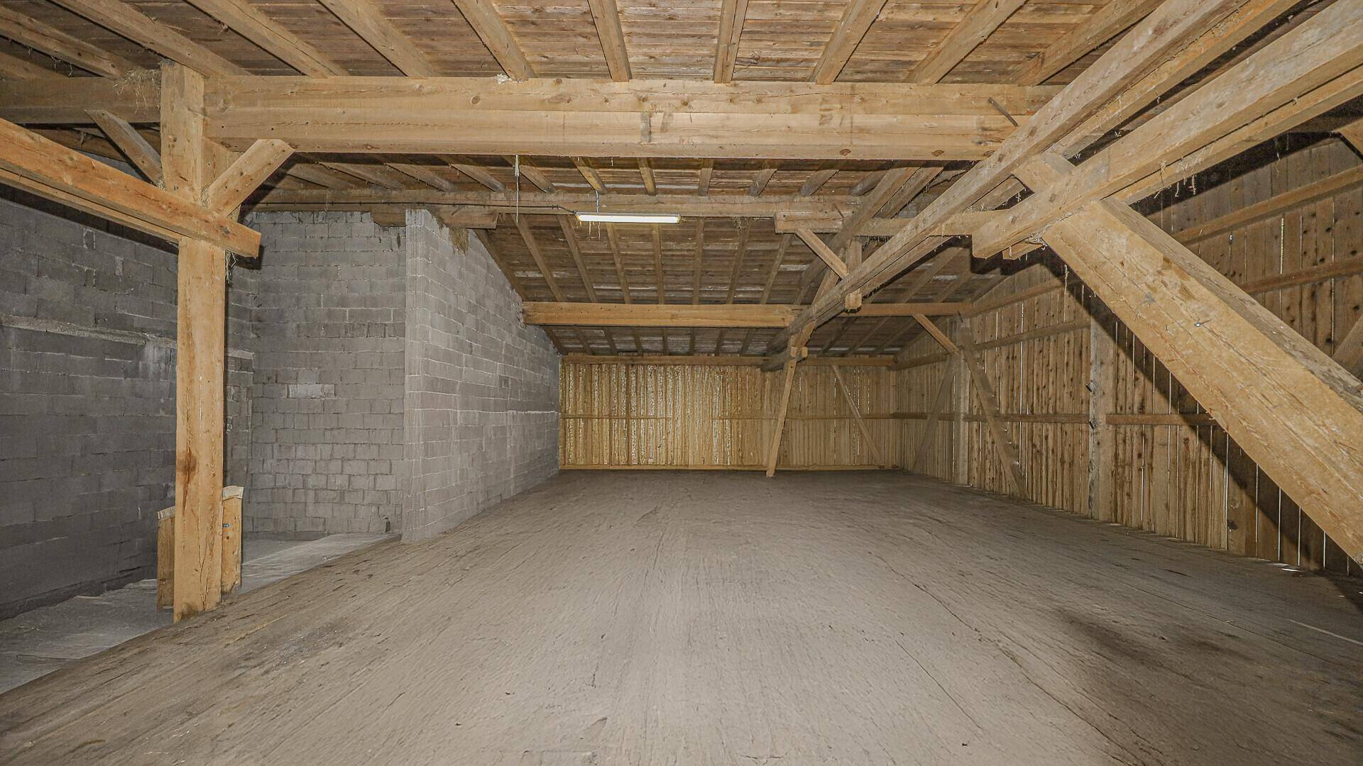 Großer, leerer Raum mit sichtbaren Holzkonstruktionen und Holzwänden, ideal als Scheune oder Lagerfläche.