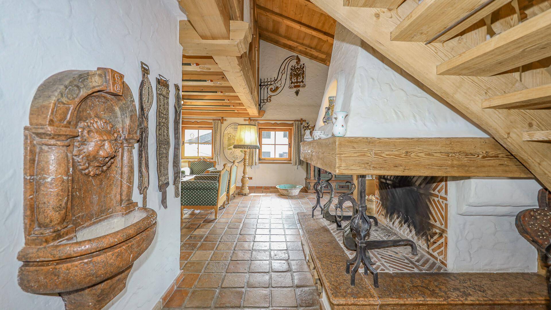 Eingangsbereich mit rustikalem Brunnen, Treppe und Fliesenboden im alpinen Stil.