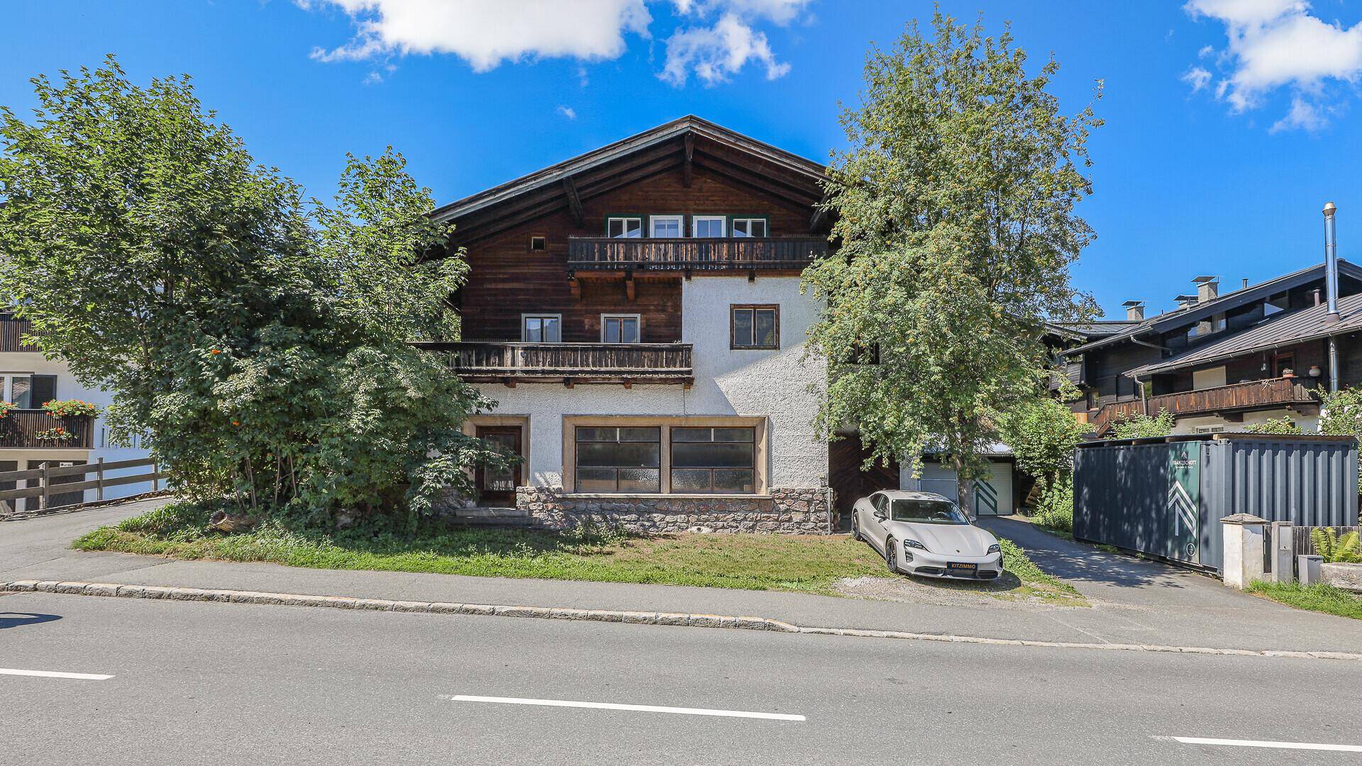 Traditionelles Haus mit Holzbalkonen und weißer Fassade, umgeben von Bäumen.