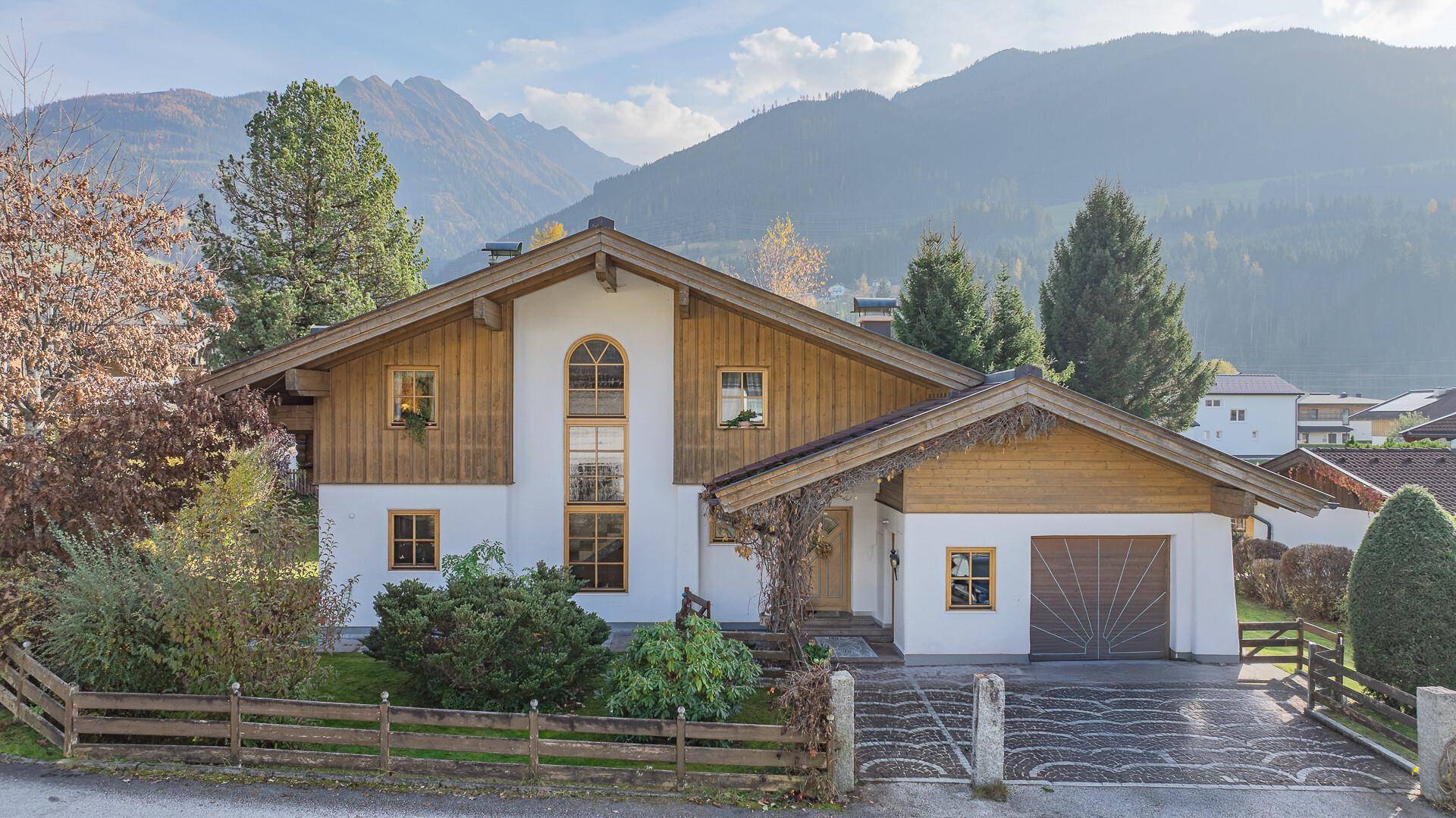 Charmantes Haus mit Holzelementen, Satteldach und gepflasterter Einfahrt vor Bergkulisse.