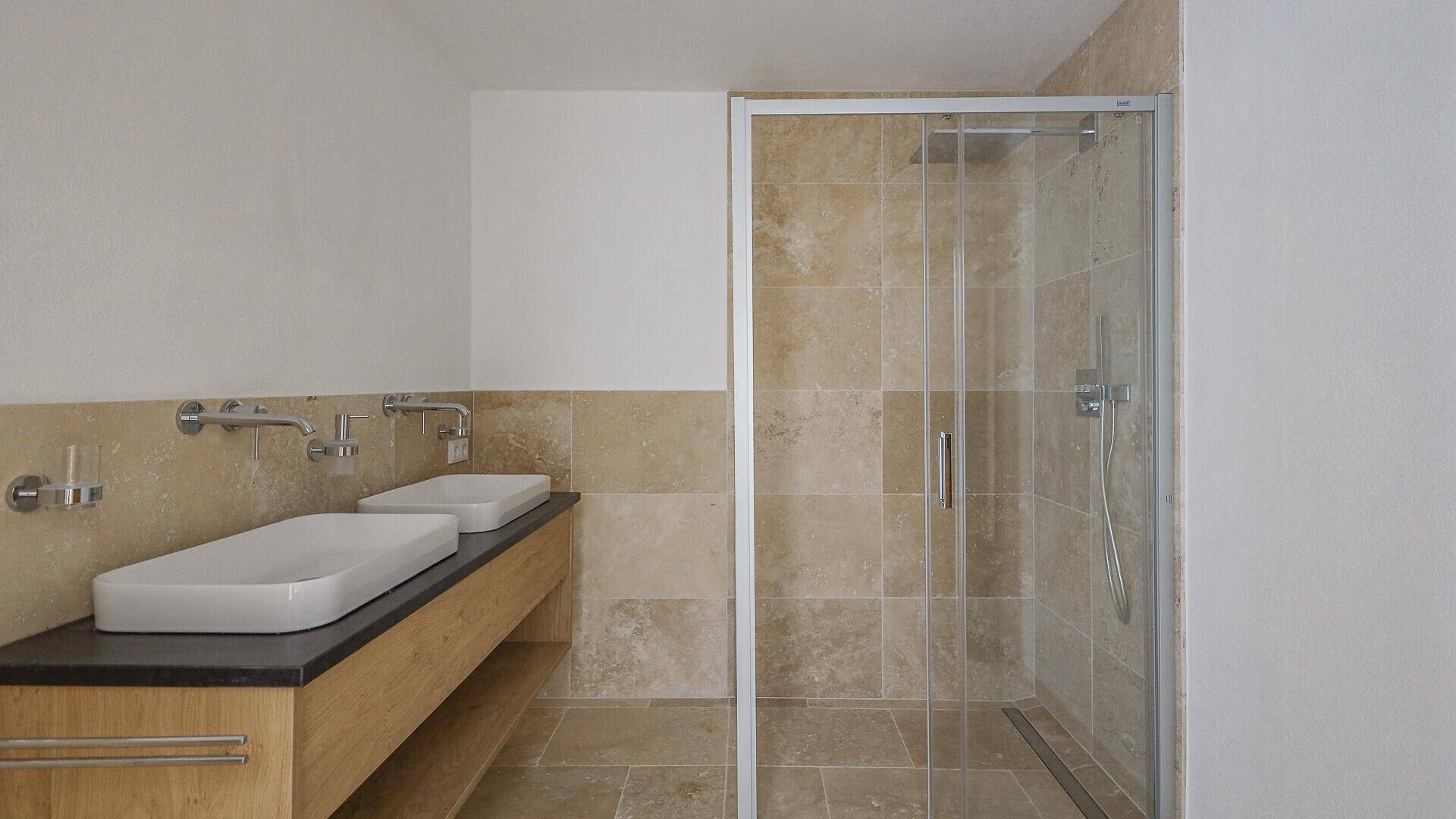 Modernes Badezimmer mit Duschkabine, Doppelwaschbecken und beigefarbenen Fliesen, funktional und stilvoll.