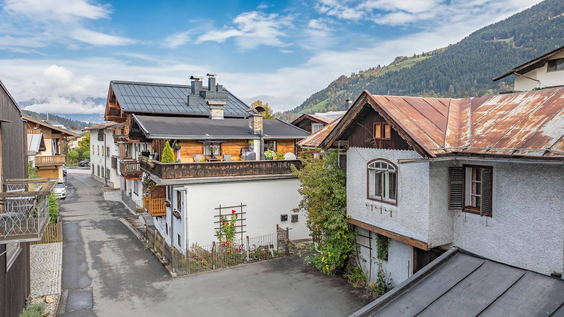 Blick auf eine ländliche Straße mit traditionellen Häusern und bewaldeten Bergen im Hintergrund.
