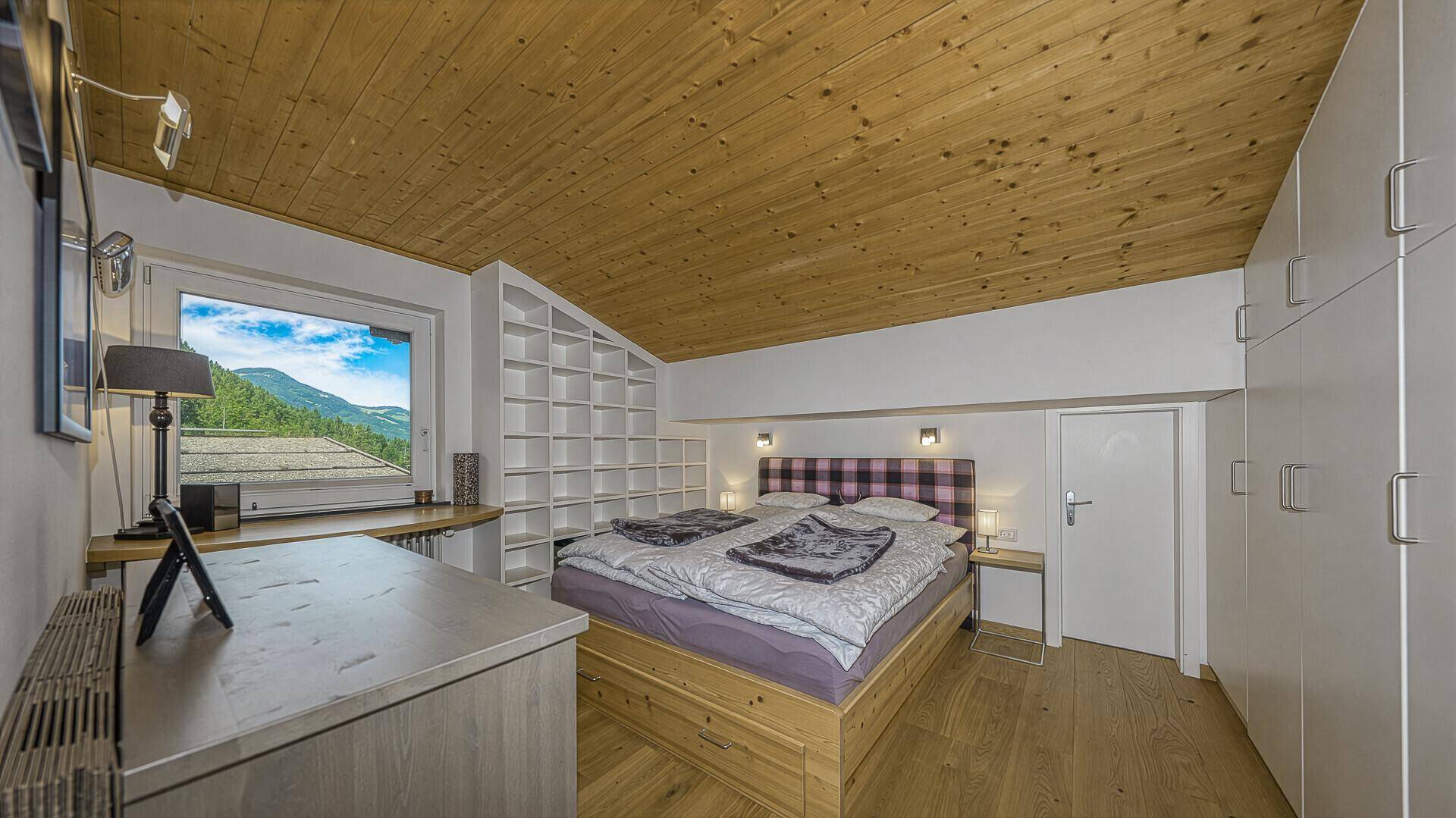 Schlafzimmer mit Doppelbett, Einbauschränken, Holzdecke und Fenster mit Bergblick.