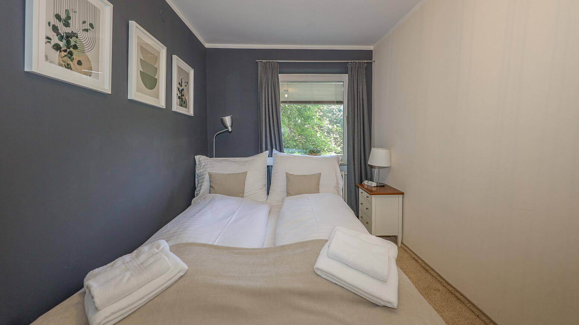 Schlafzimmer mit Doppelbett, grauer Akzentwand und Fenster mit Blick ins Grüne.