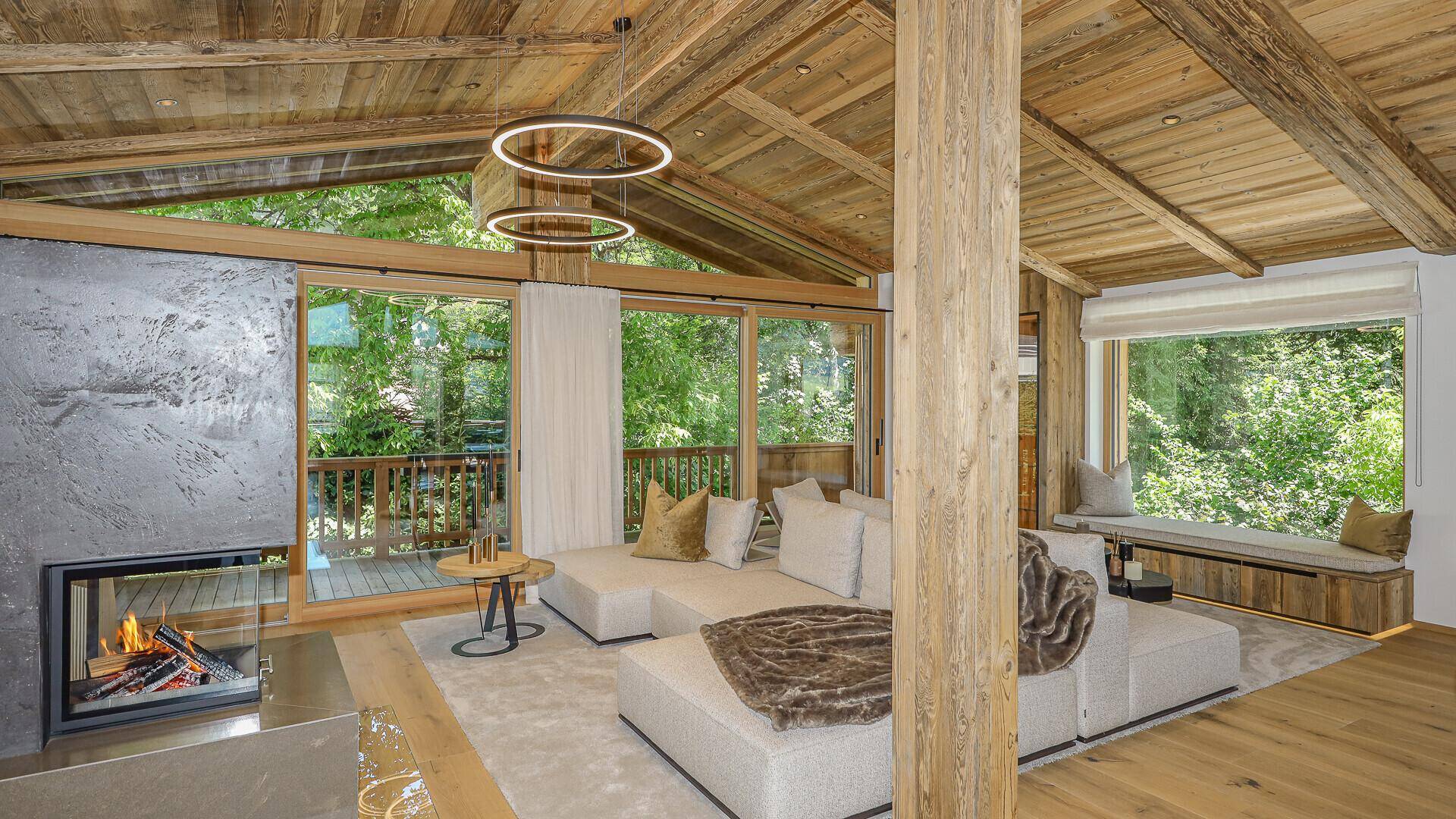 Gemütlicher Wohnbereich mit Kamin, großen Fenstern und Zugang zum Balkon mit Waldblick.