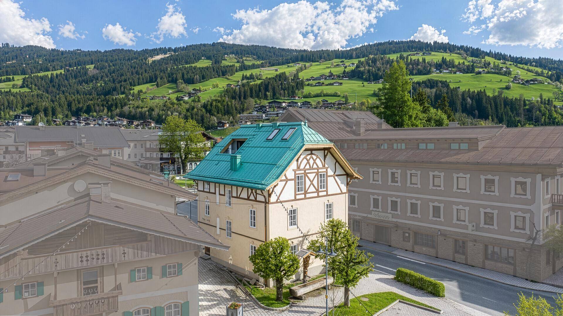 Traditionelles Gebäude im alpinen Stil mit grünem Dach und Fachwerkelementen in einer malerischen Berglandschaft.