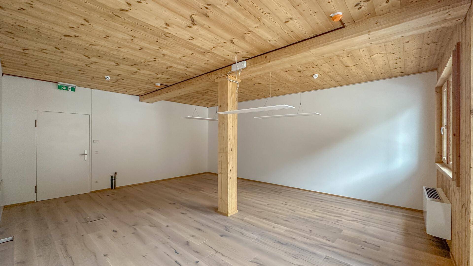 Unmöblierter Innenraum mit Holzboden, Holzbalkendecke und einer Kombination aus Holz- und weißen Wänden.