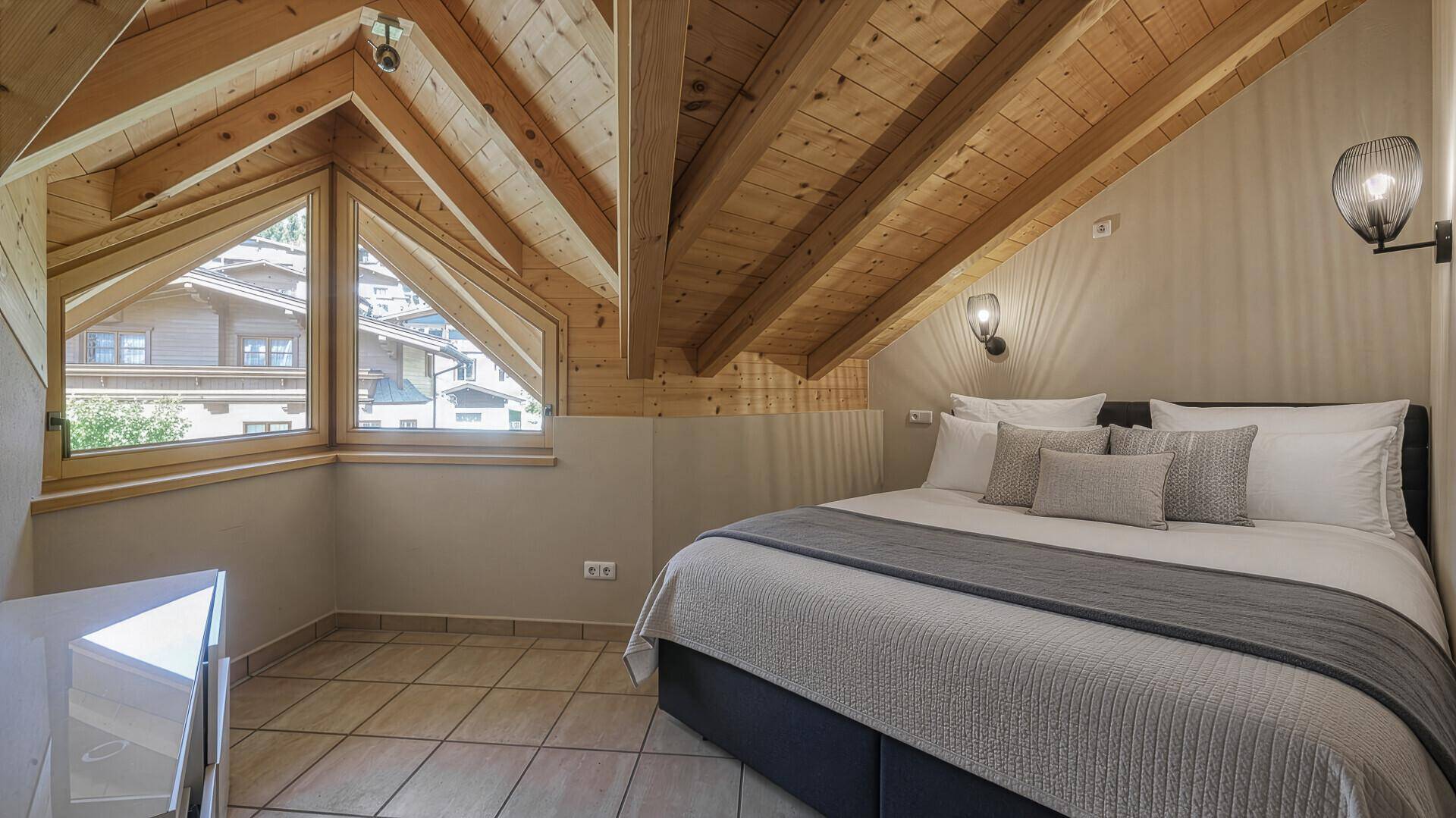 Gemütliches Dachschlafzimmer mit sichtbaren Holzbalken und schrägen Fenstern für viel Licht.