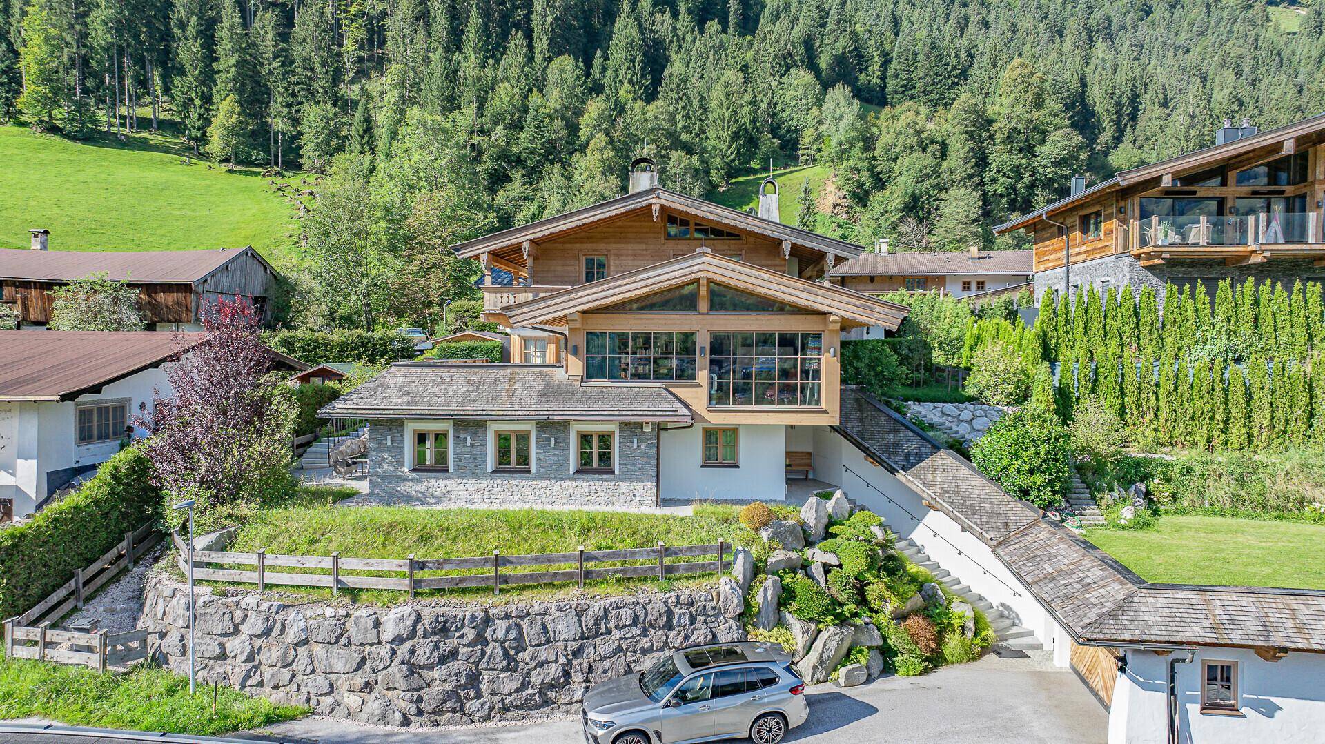 Charmantes Bergchalet mit Holzfassade und Steinelementen, umgeben von grünen Hängen und Bäumen.