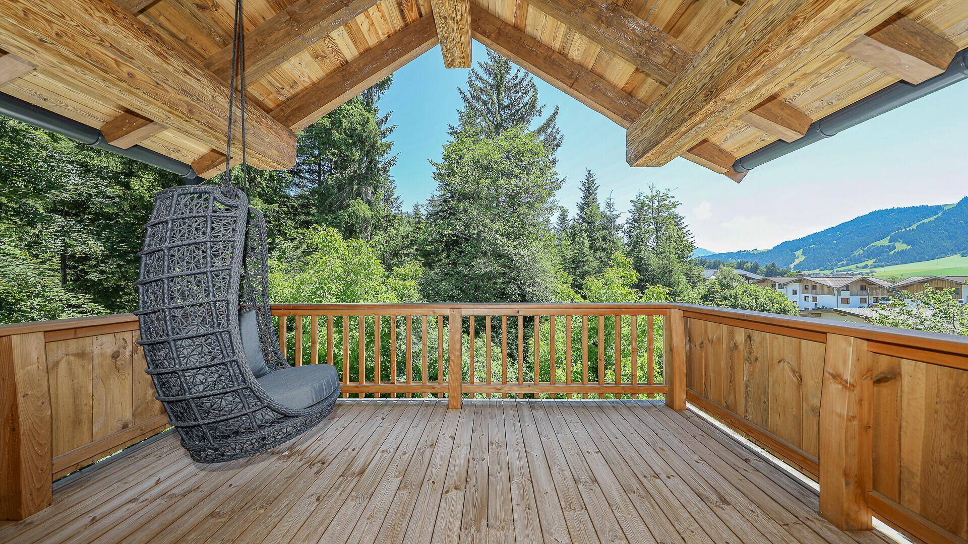 Überdachter Balkon mit Hängesessel und idyllischem Blick auf die grünen Wälder.