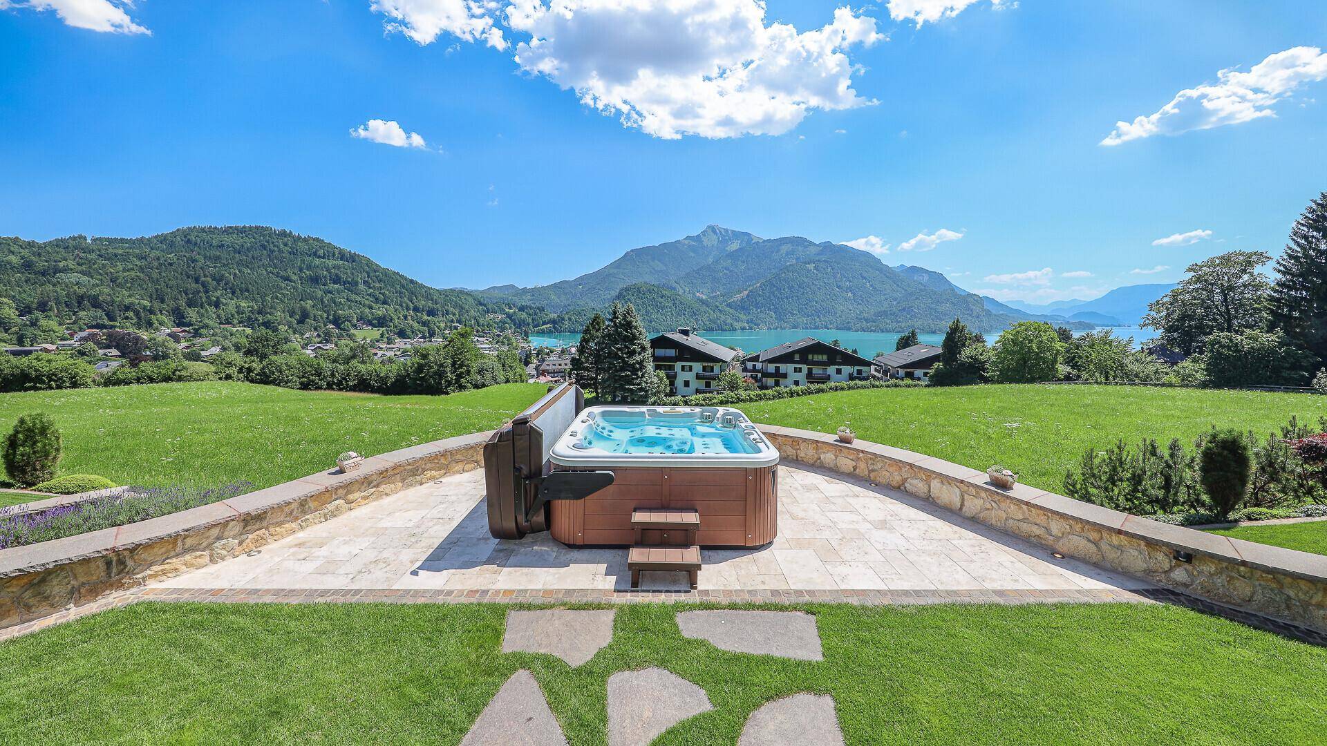 Außenwhirlpool auf einer gepflasterten Terrasse mit weitem Blick auf die grüne Landschaft und den See.