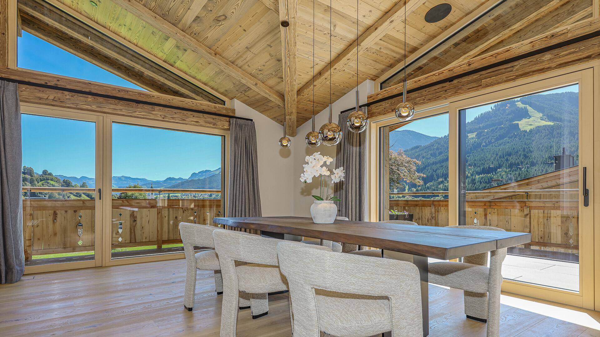 Eleganter Essbereich mit Holztisch, modernen Stühlen und Zugang zu einem Balkon mit Bergblick.