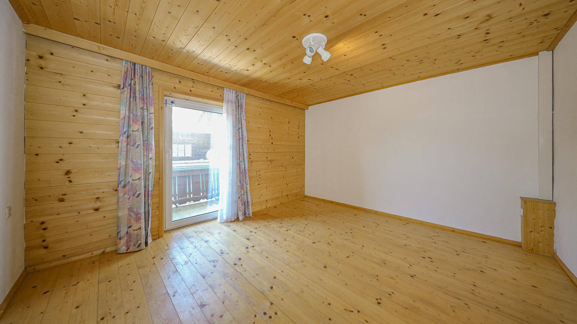 Schlafzimmer mit Holzvertäfelung, Holzdielenboden und Balkonzugang mit Blick auf die Berge.