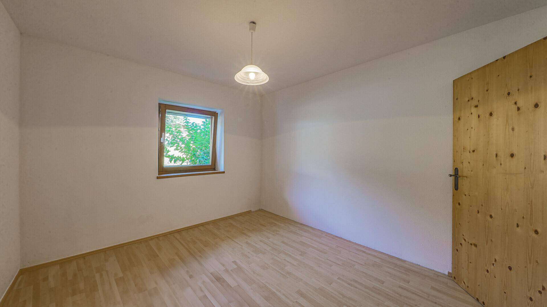Heller, leerer Raum mit Holzboden, Fenster und einer Holztür.