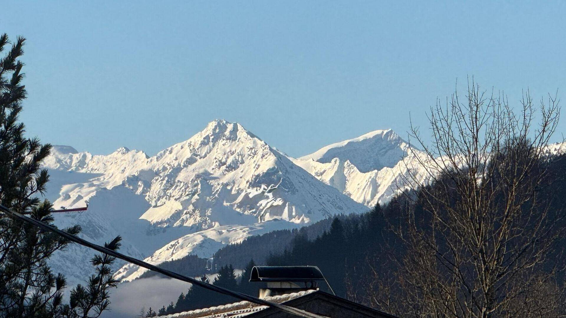 Majestätische schneebedeckte Berggipfel unter klarem blauem Himmel, sichtbar über Dächern.