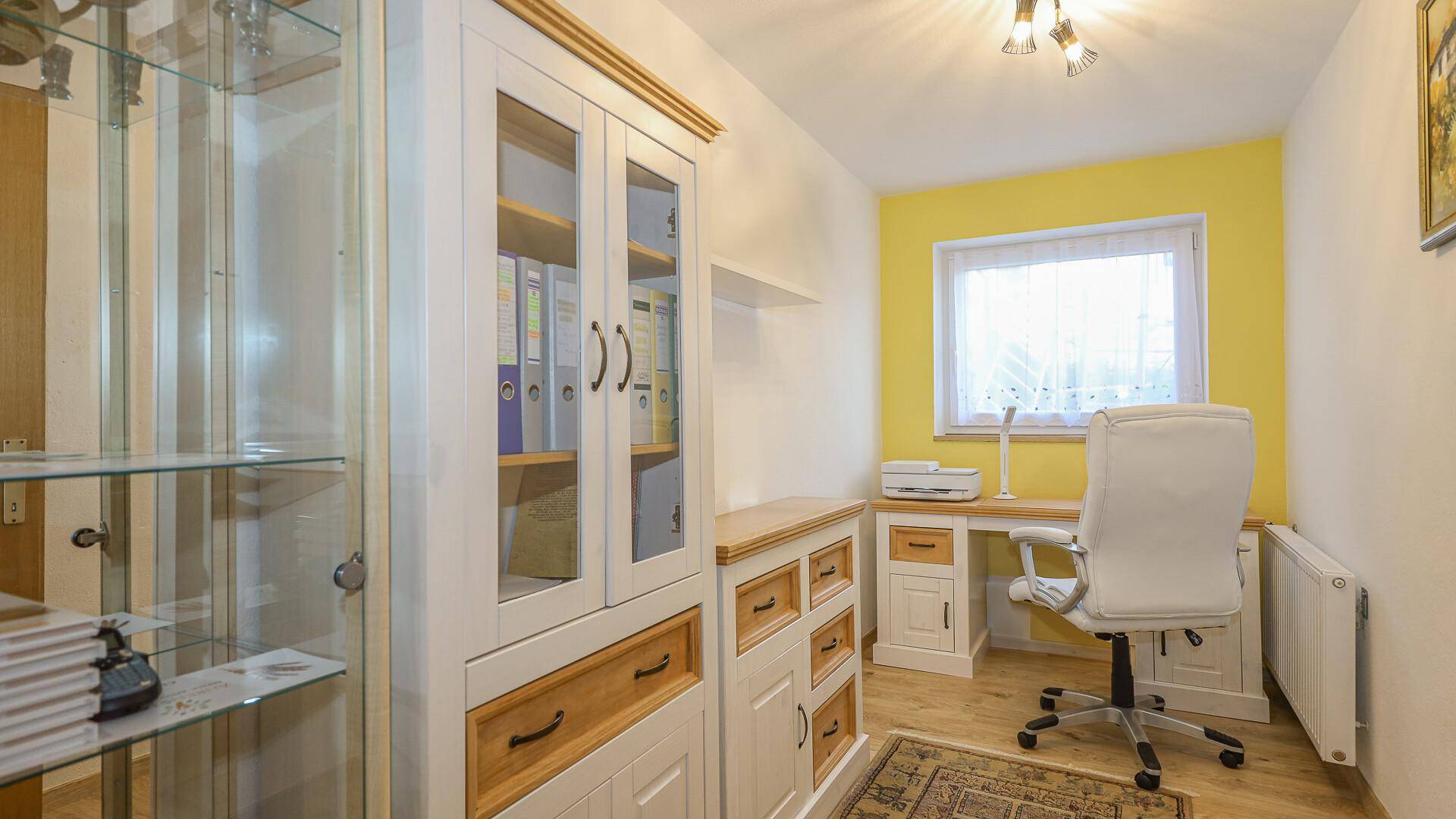 Helles Arbeitszimmer mit gelber Wand, Holzmöbeln und einem Fenster mit Vorhängen.