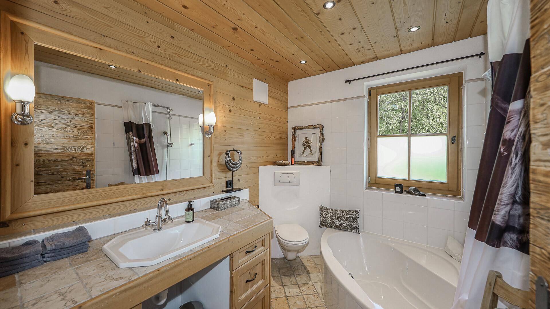 Traditionelles Badezimmer mit Badewanne, Holzdecke und Waschbecken mit großem Spiegel.