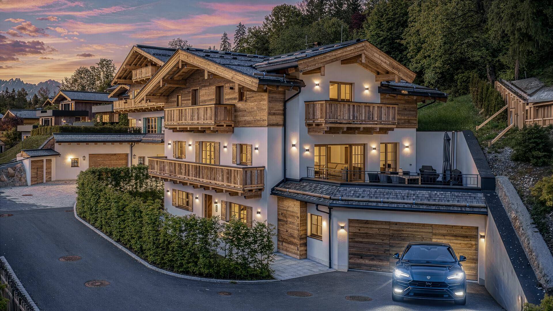 Luxuriöses Chalet im alpinen Stil mit Holzfassade, mehreren Balkonen und einer möblierten Terrasse bei Sonnenuntergang.