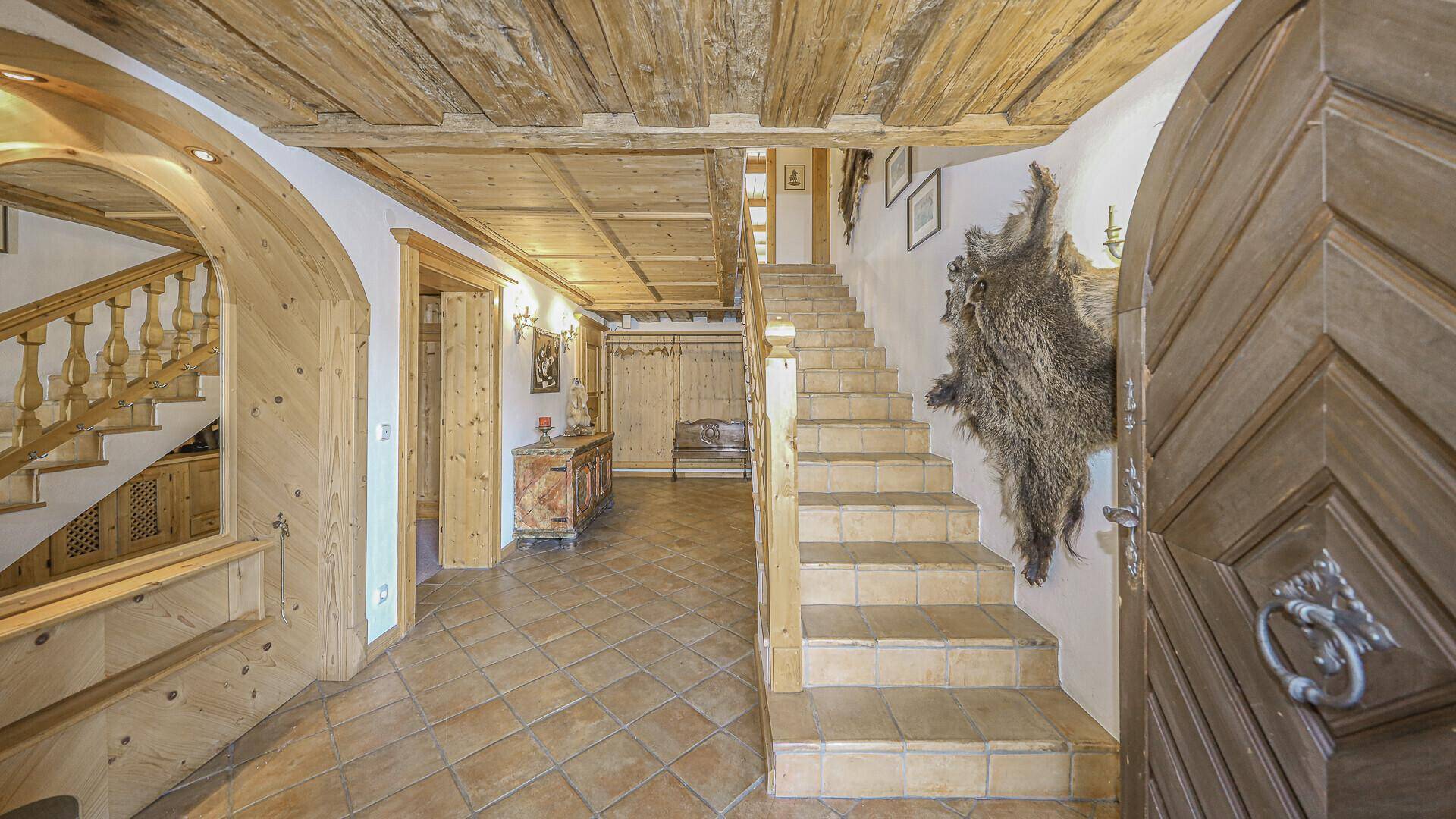Geräumiger Eingangsbereich mit Holztreppe, Fliesenboden und traditionellen Holzelementen.