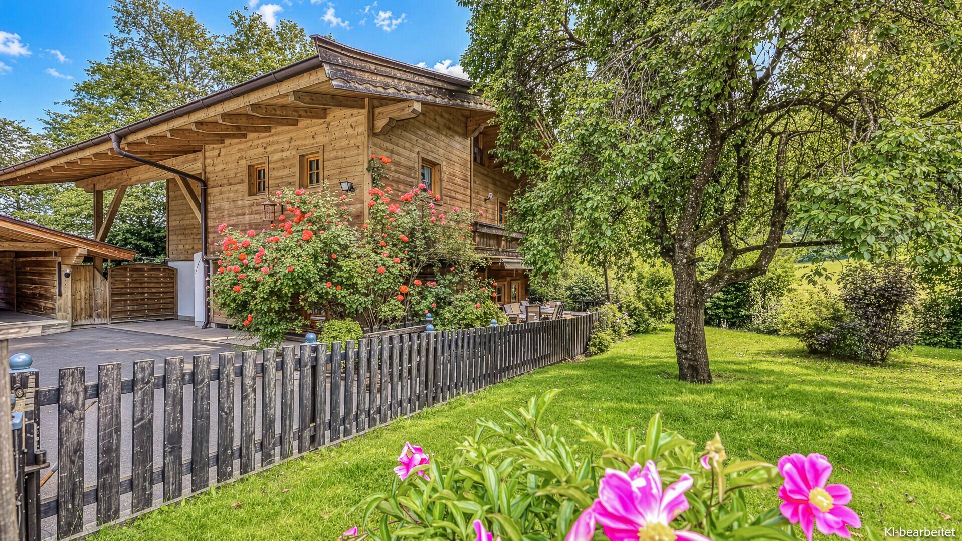 Seitlicher Blick auf das Holzhaus mit blühenden Rosensträuchern und einem gepflegten Rasenbereich.