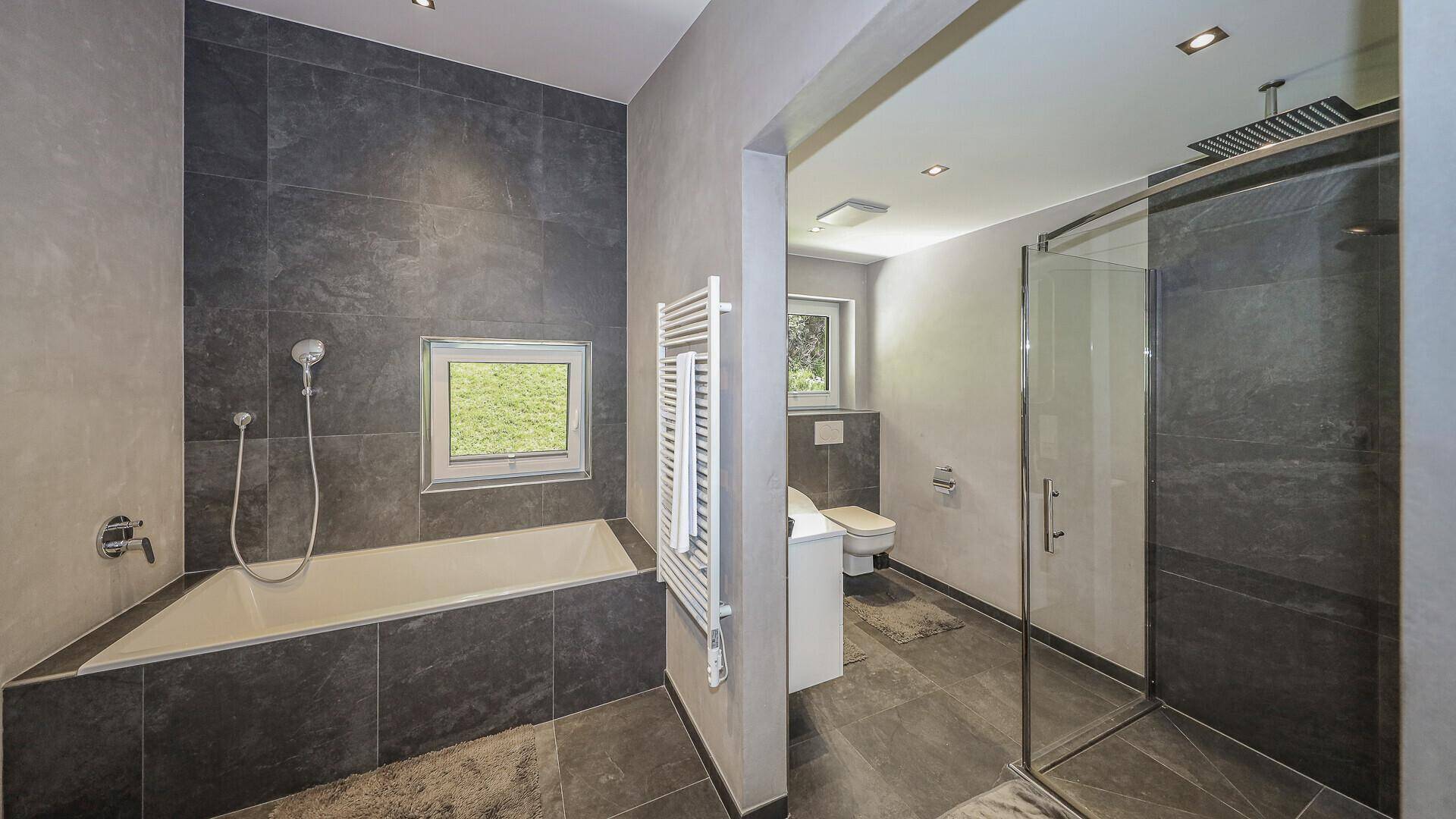 Modernes Badezimmer mit dunklen Fliesen, Badewanne und separater Duschkabine.