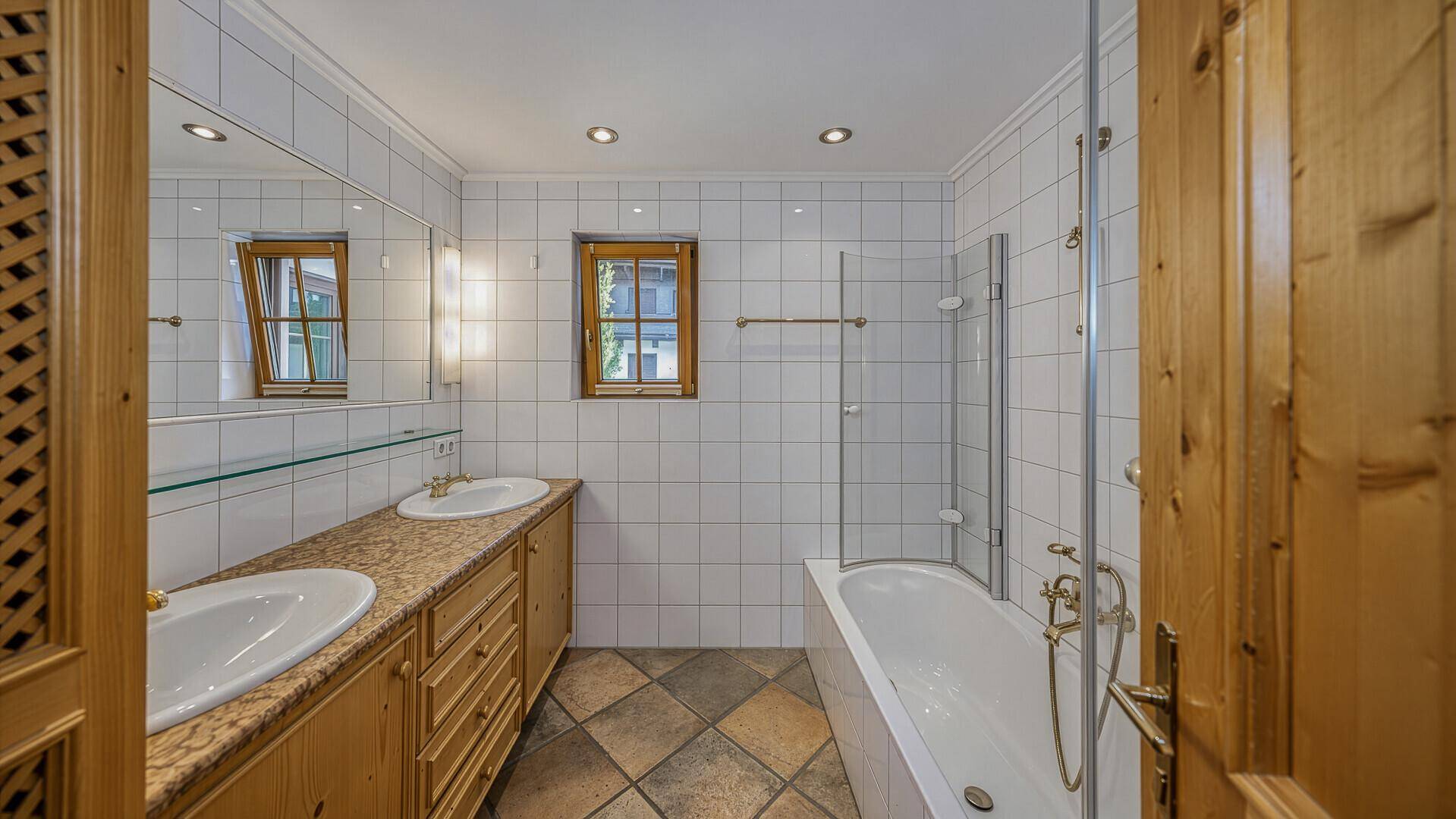 Helles Badezimmer mit zwei Waschbecken, Badewanne mit Duschfunktion und traditionellen Fliesen.