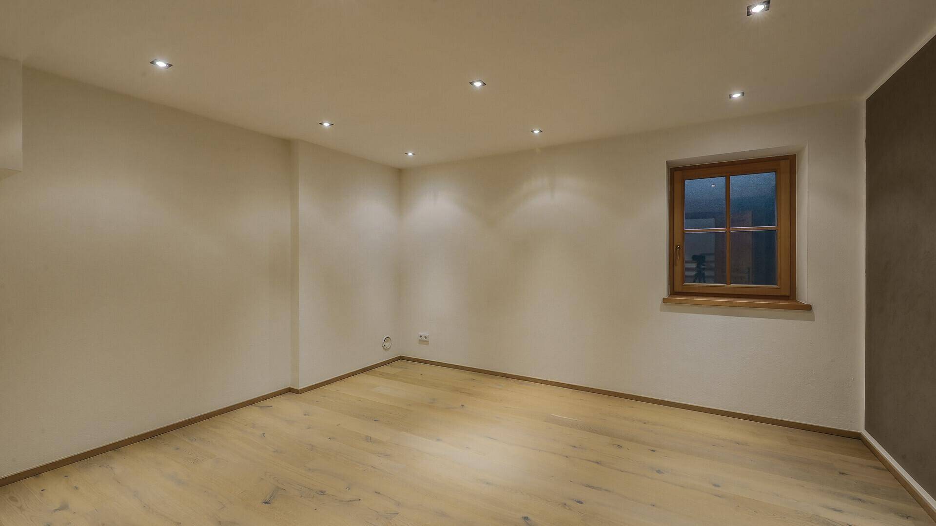 Leerer Raum mit hellem Holzboden, weißen Wänden und einem Fenster für natürliches Licht.