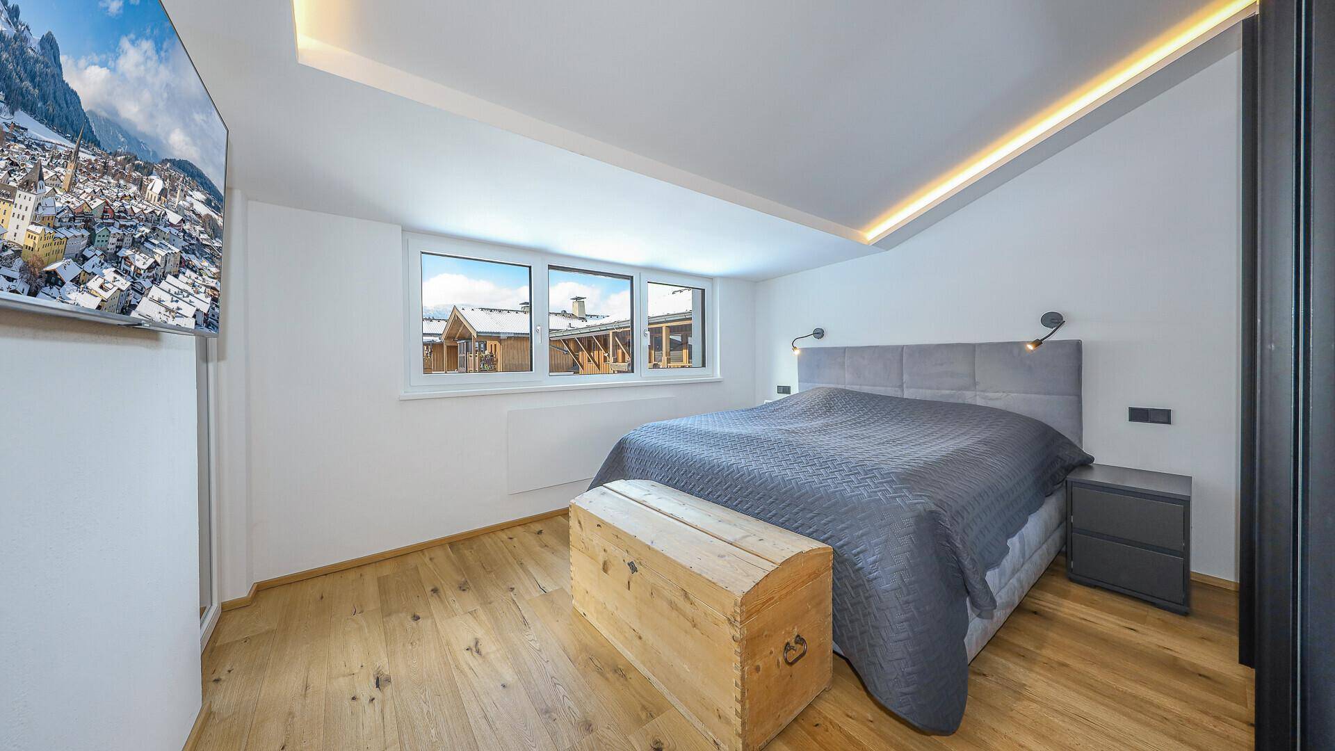 Helles Schlafzimmer mit Holzboden, großem Bett und Blick auf die verschneite Umgebung.