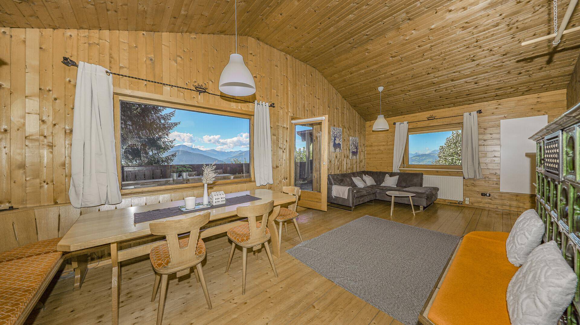 Gemütlicher Wohn-Essbereich mit Holzwänden, großen Fenstern und Blick auf die Berge.