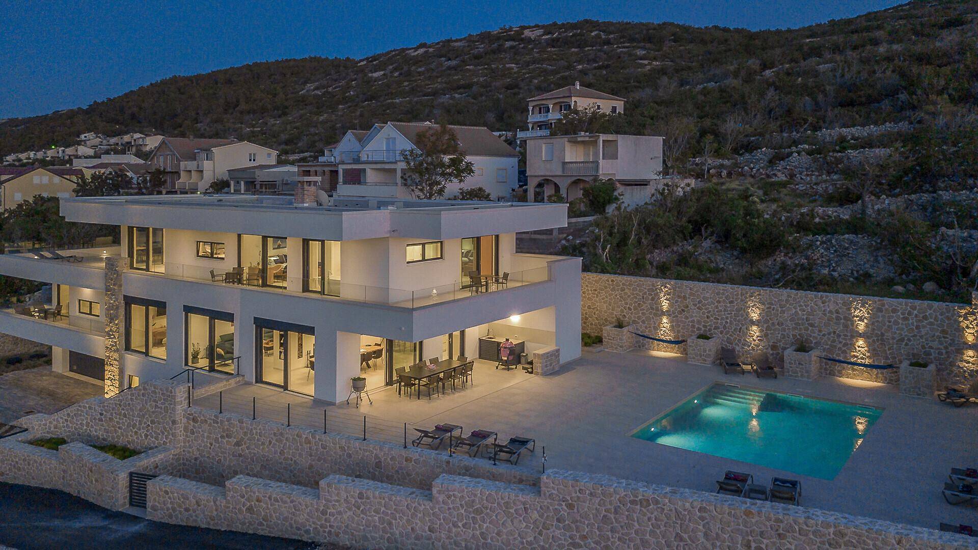 Die moderne Villa bei Nacht, mit beleuchtetem Poolbereich und umliegenden Hügeln.