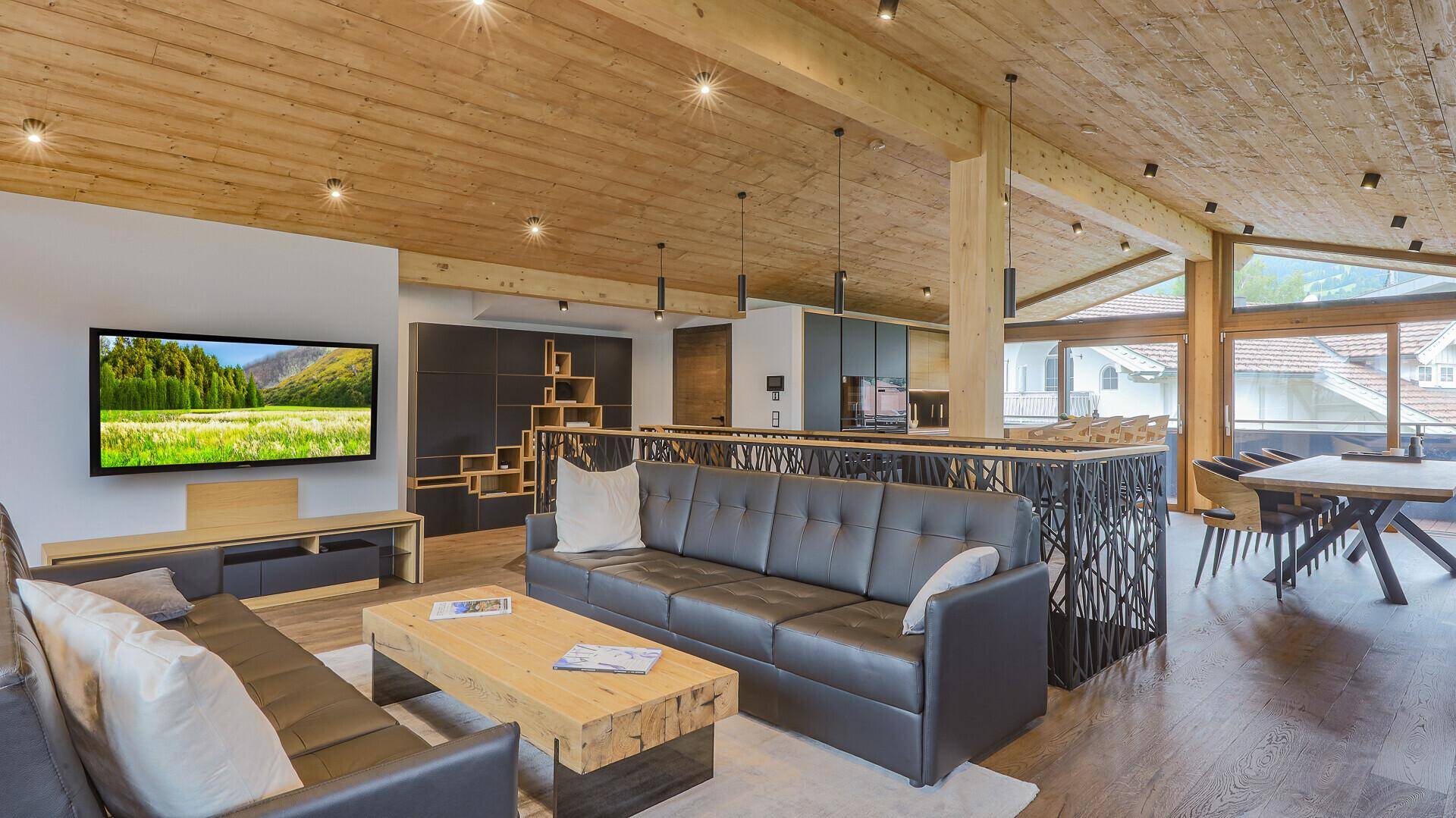 Geräumiger Wohn- und Essbereich mit Holzbalkendecke, modernen Möbeln und großem Fernseher.