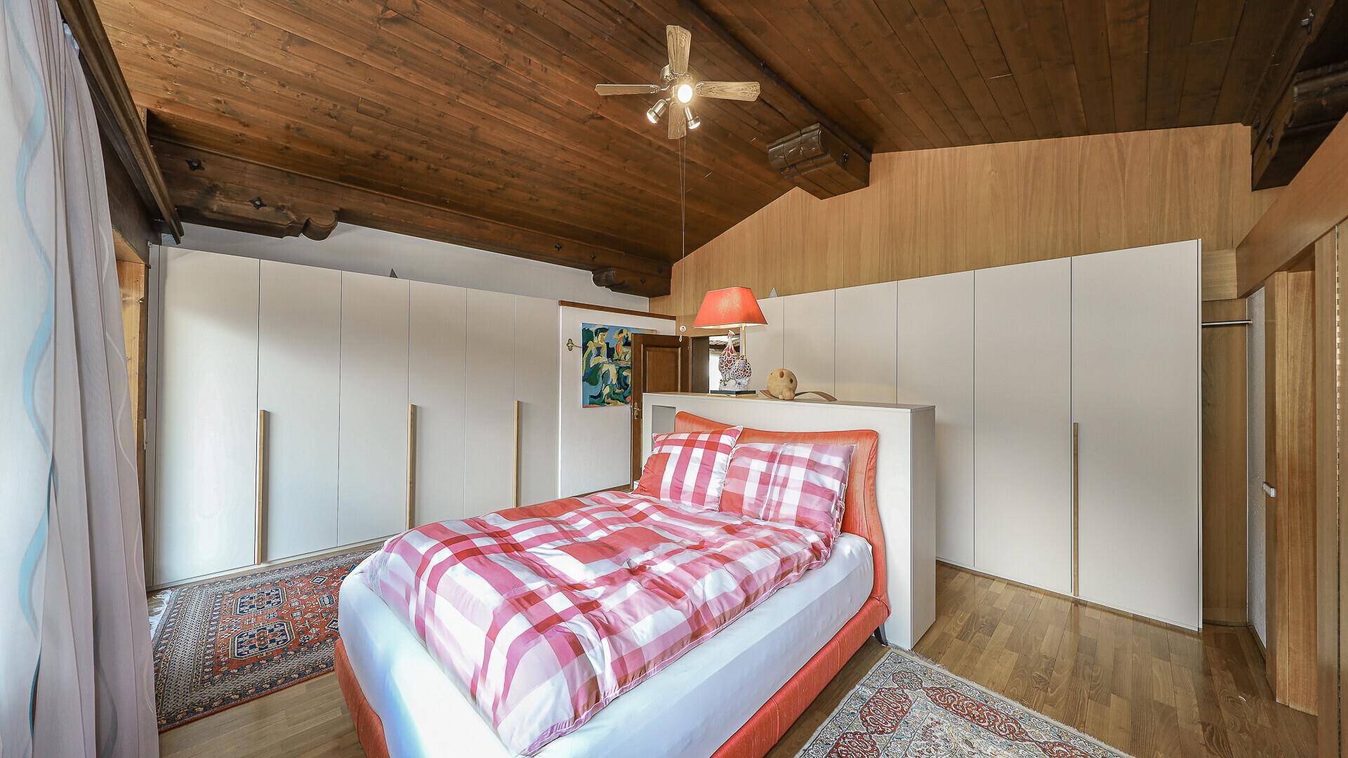 Helles Schlafzimmer mit Holzbalkendecke, Einbauschränken und Parkettboden.