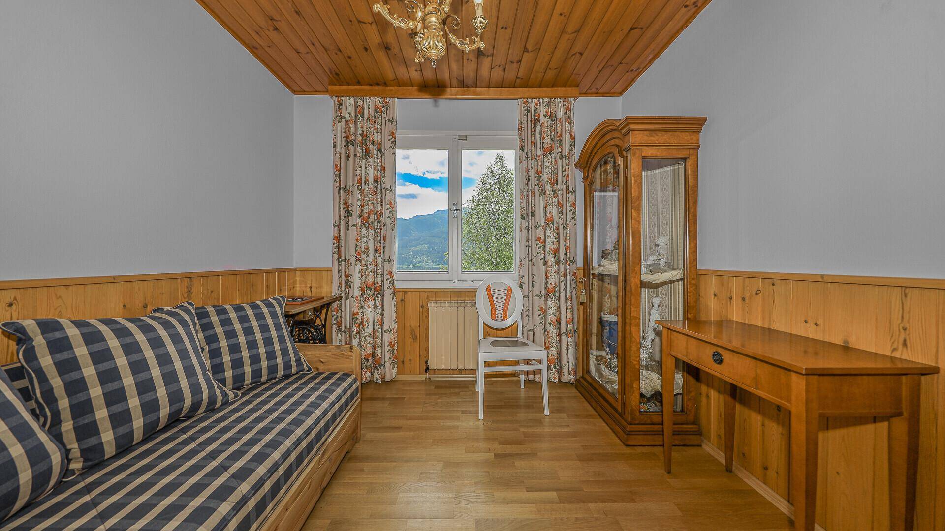 Schlafzimmer mit Holzdecke, Parkettboden, traditionellen Möbeln und Bergblick durch das Fenster.