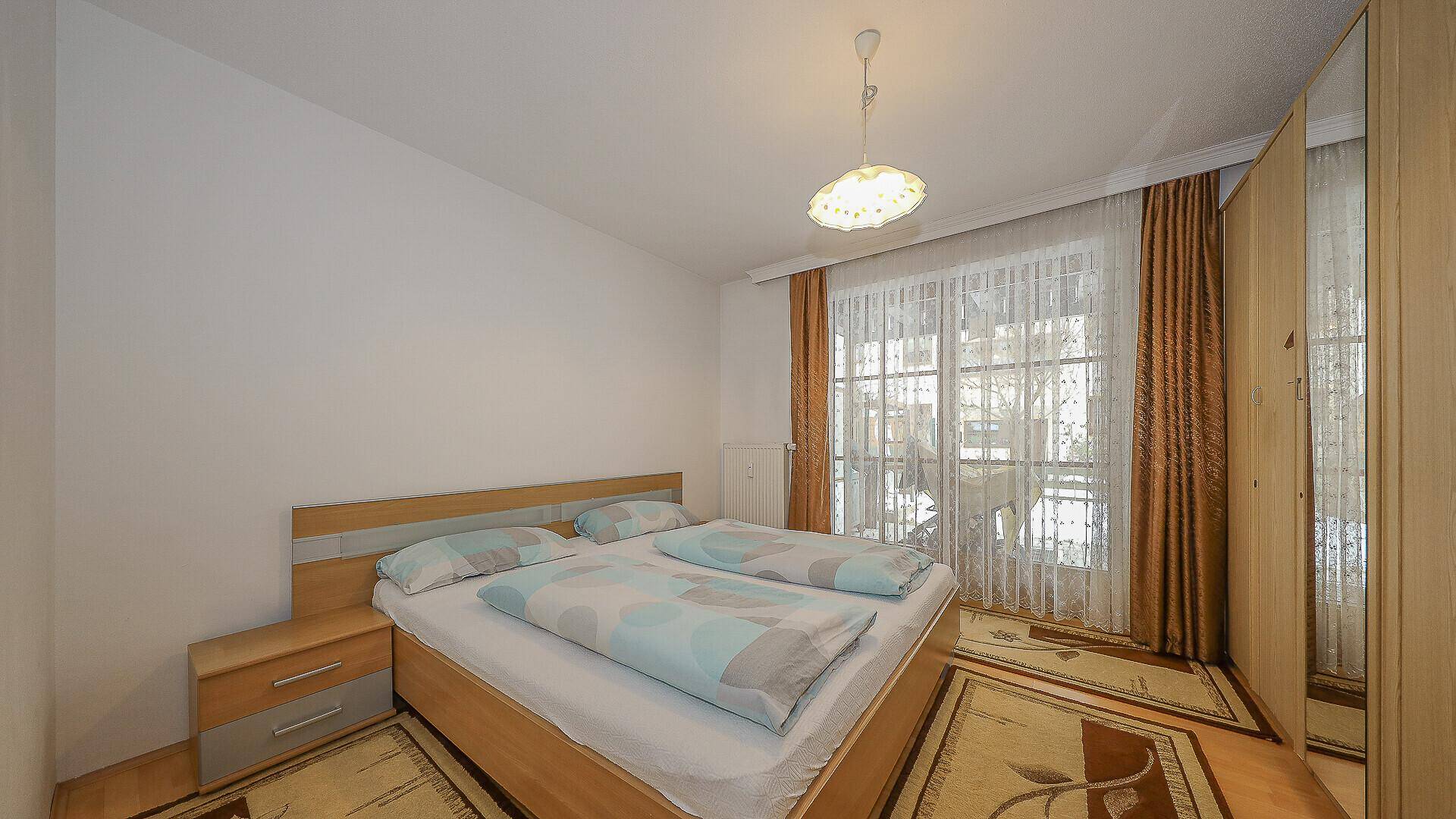 Schlafzimmer mit Doppelbett, Kleiderschrank und Zugang zum Balkon.