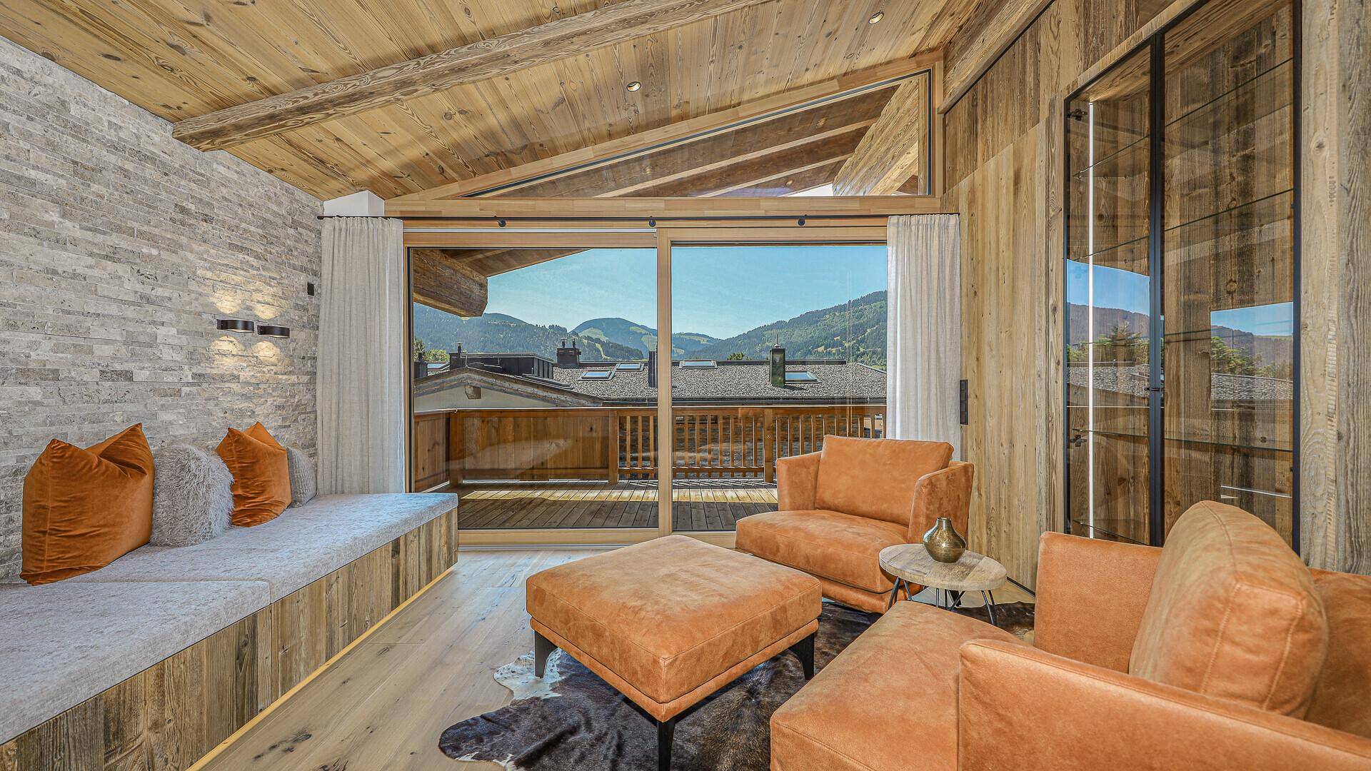 Gemütlicher Wohnbereich mit Sitzbank, Holzwänden und großen Fenstern mit Bergblick.