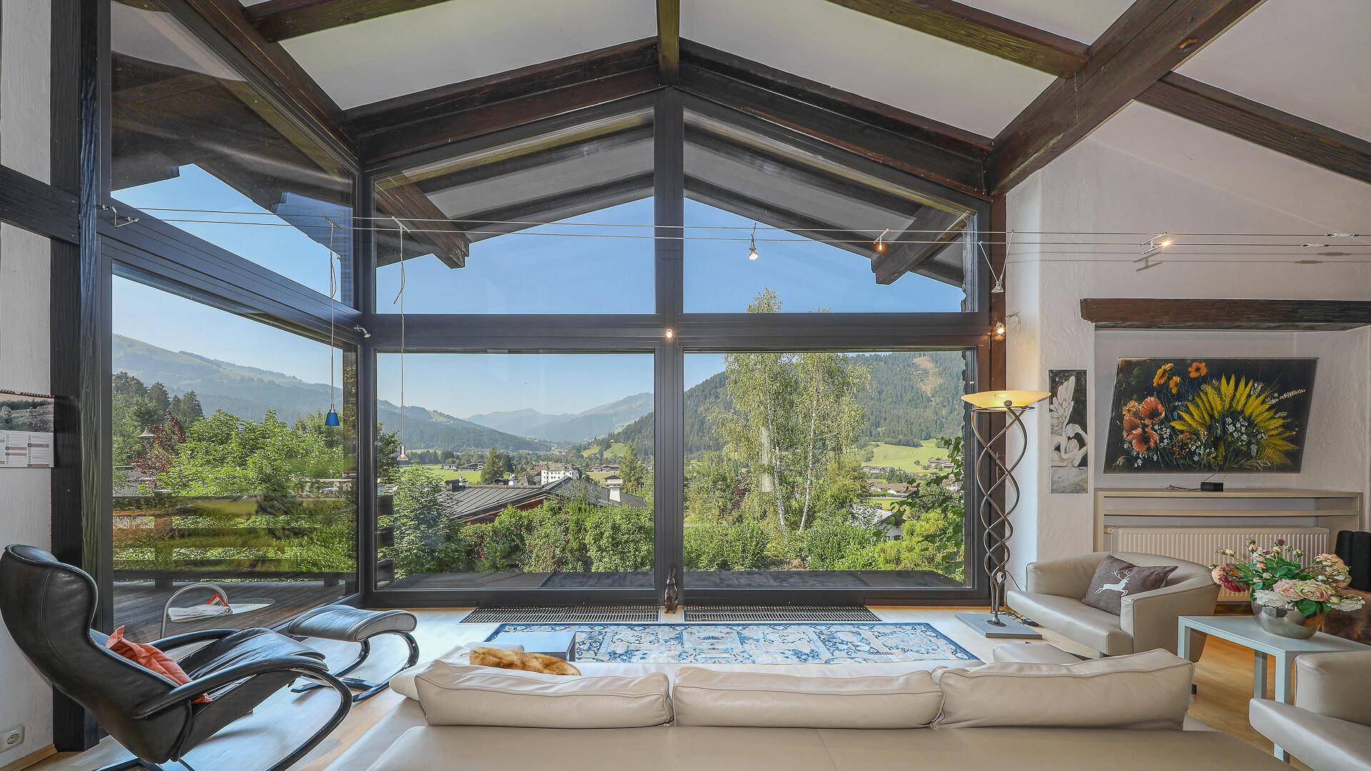 Geräumiges Wohnzimmer mit großen Fenstern, die einen weiten Blick auf die alpine Landschaft ermöglichen.
